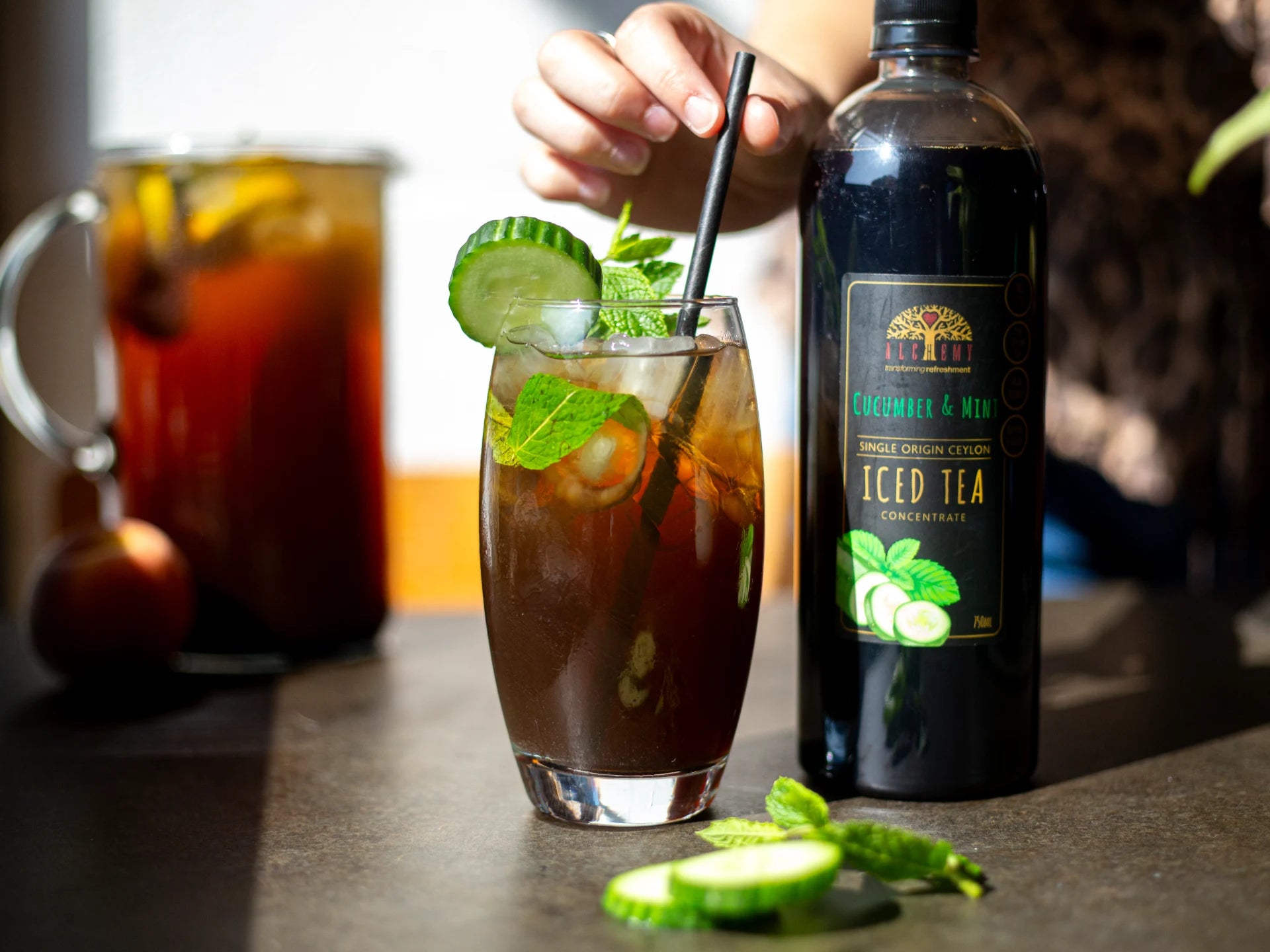 Glass of Alchemy iced tea with a bottle of iced tea and a pitcher in the background.