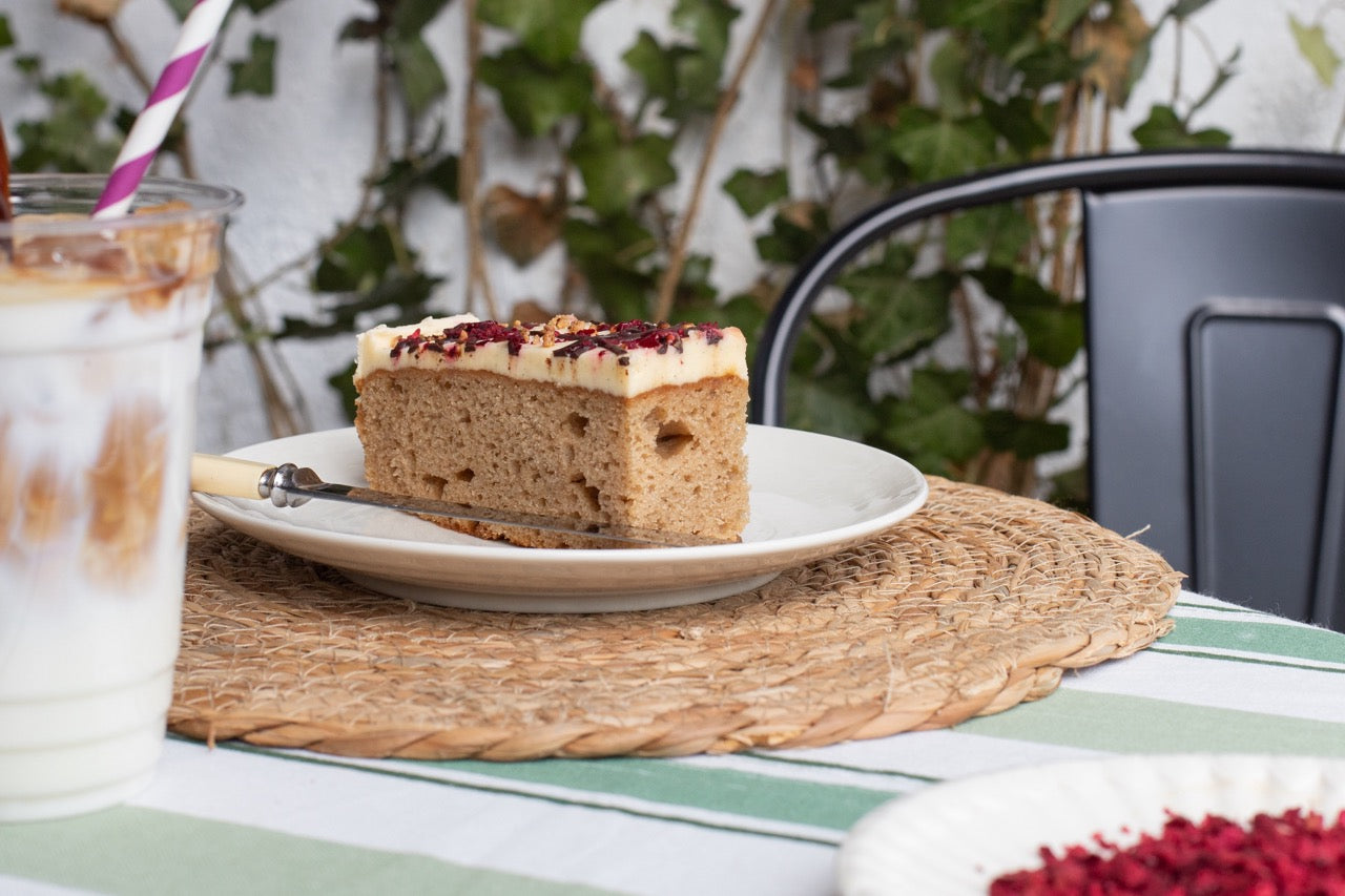 Slice of Banana Split cake on a plate with a glass of iced coffee on a table outdoors.