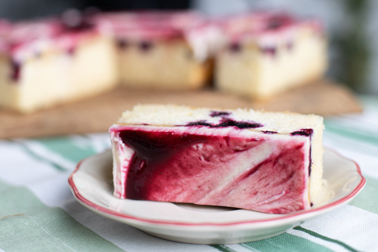 Slice of layered Blackcurrant Ripple cake with red and white filling on a plate, blurred background