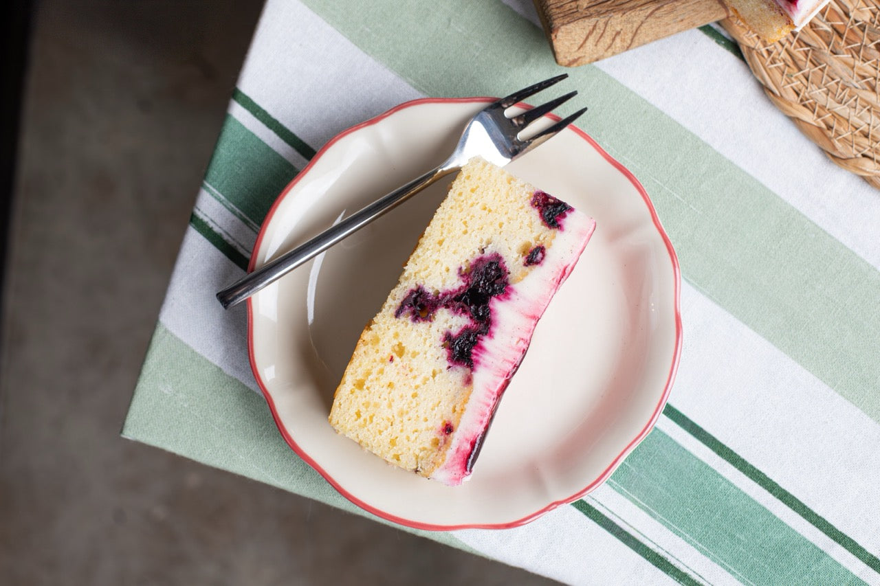 Slice of Blackcurrant Ripple cake with berries on a plate with a fork, placed on a green and white striped tablecloth.