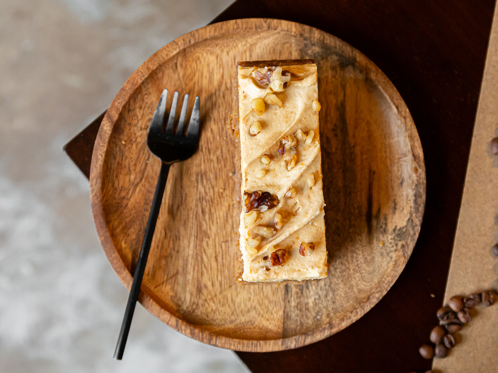 Rectangular Coffee Pecan Walnut Cake with nuts on a wooden plate with a fork, on a textured surface.