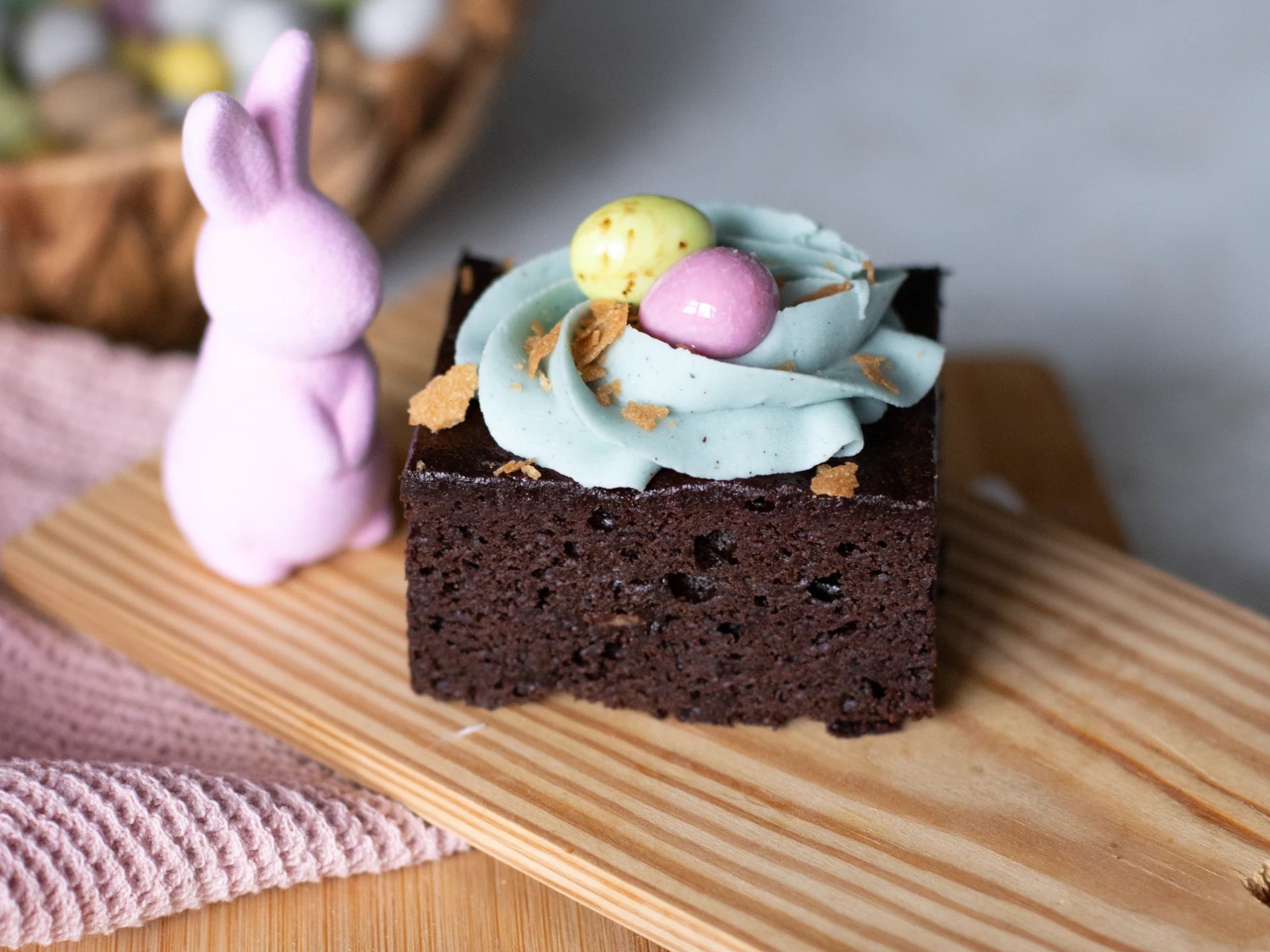 Chocolate Easter Nest Cake with mint frosting and Easter eggs on a wooden board with a pink bunny figure.