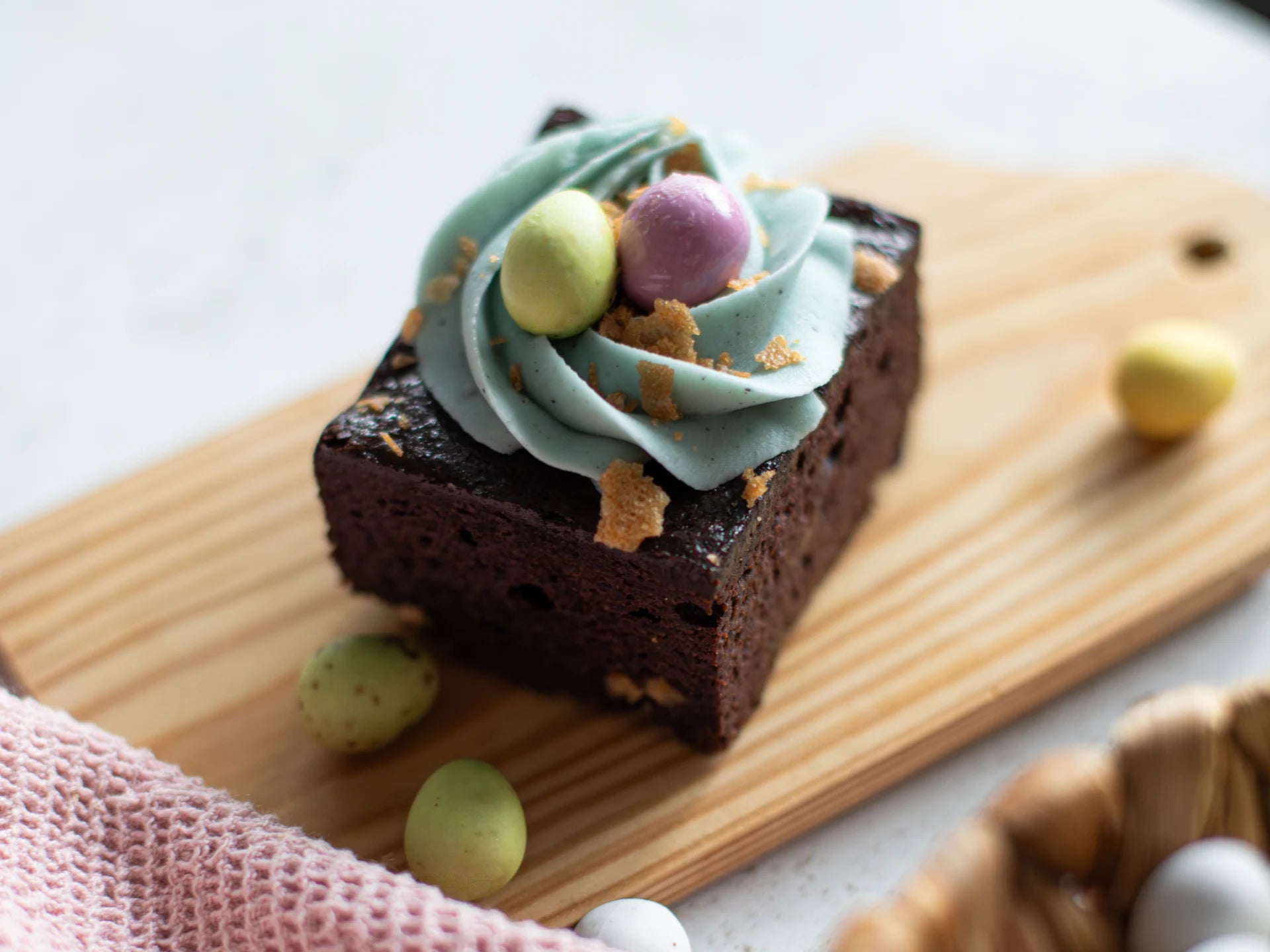 Chocolate Easter Nest Cake with blue frosting and colorful candies on a wooden board.
