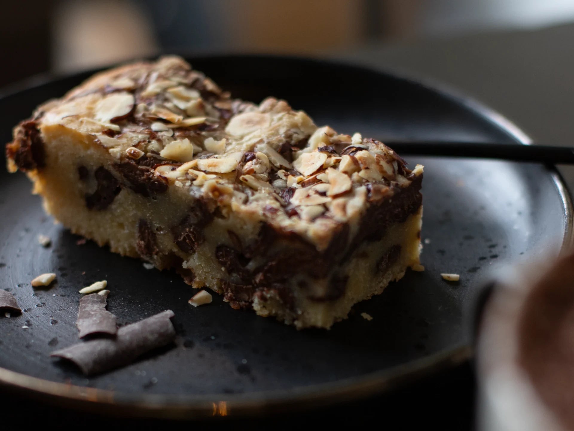 Slice of Hazelnut Blondie cake with chocolate and nuts on a dark plate
