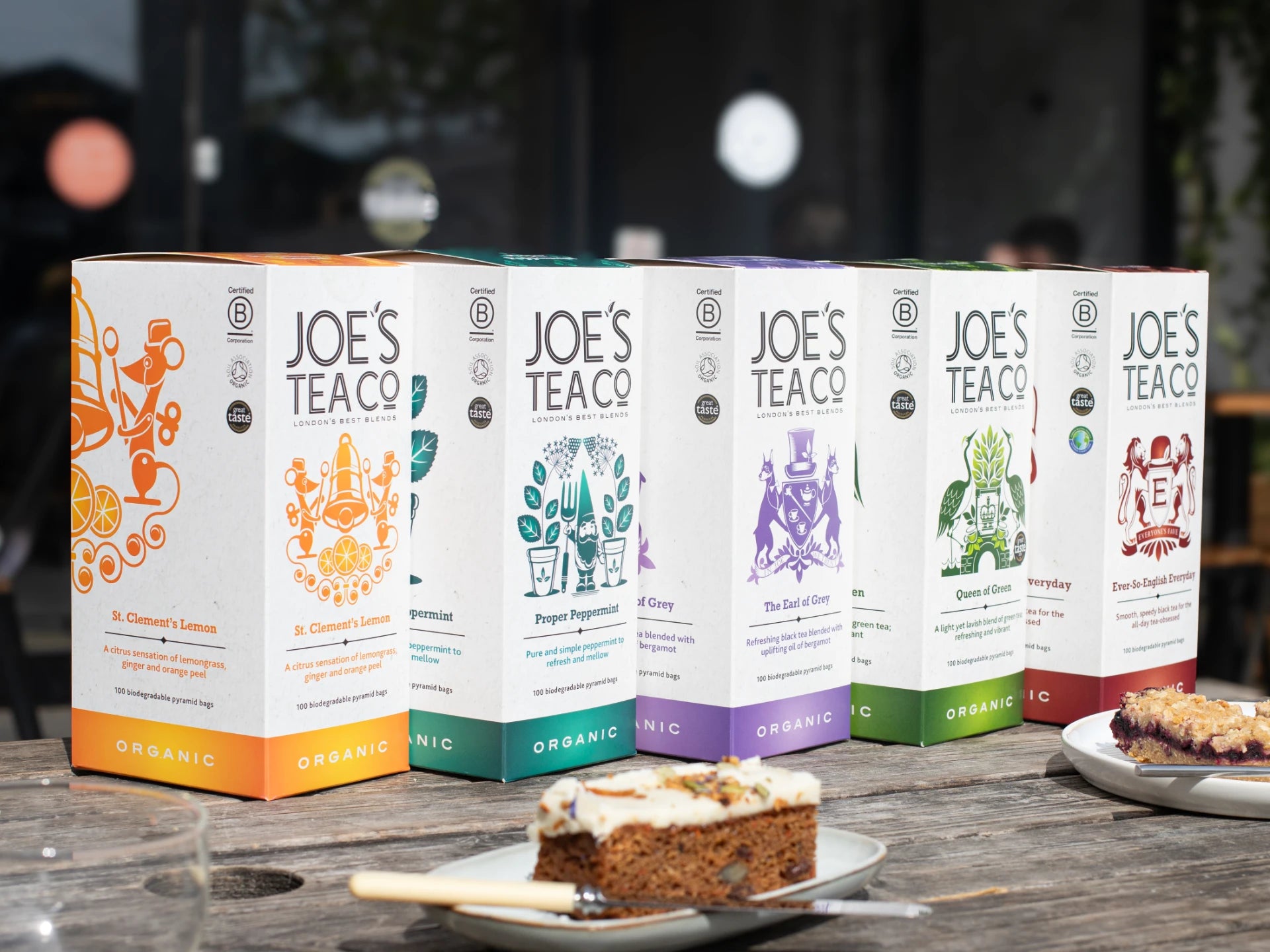 Row of Joe's Tea Co. tea boxes on a wooden table with a cake in the foreground.