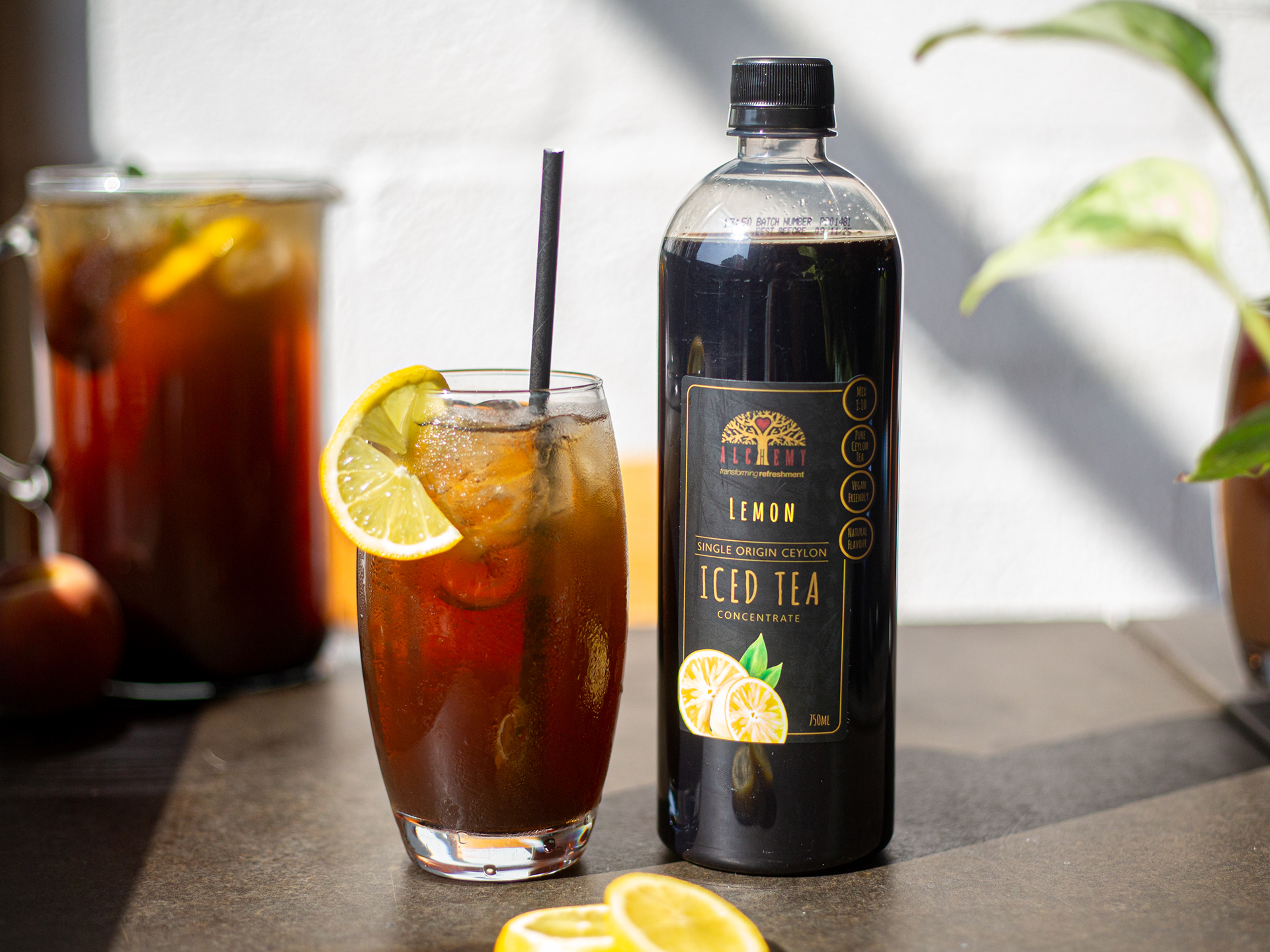 Bottle of Alchemy lemon iced tea concentrate with a glass of iced tea and lemon slices on a table.