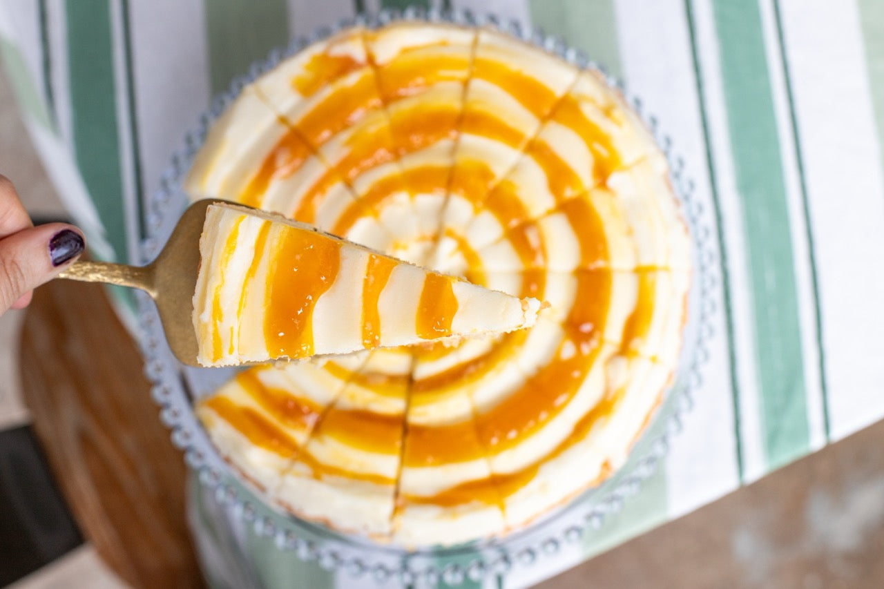 Mango Pineapple Coconut cake with caramel drizzle being lifted from a whole cheesecake on a green plate.