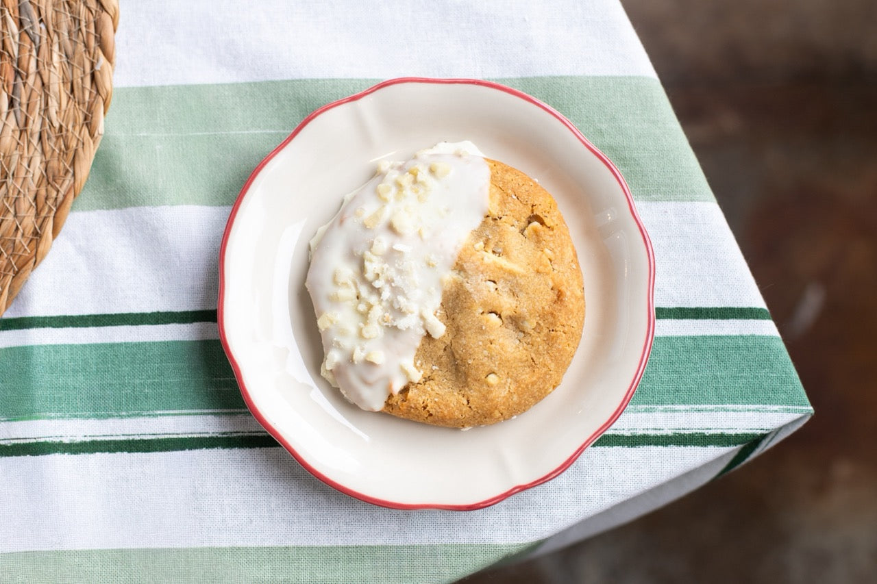Miso Cookies with white frosting on a red rimmed plate on a green and white striped tablecloth.