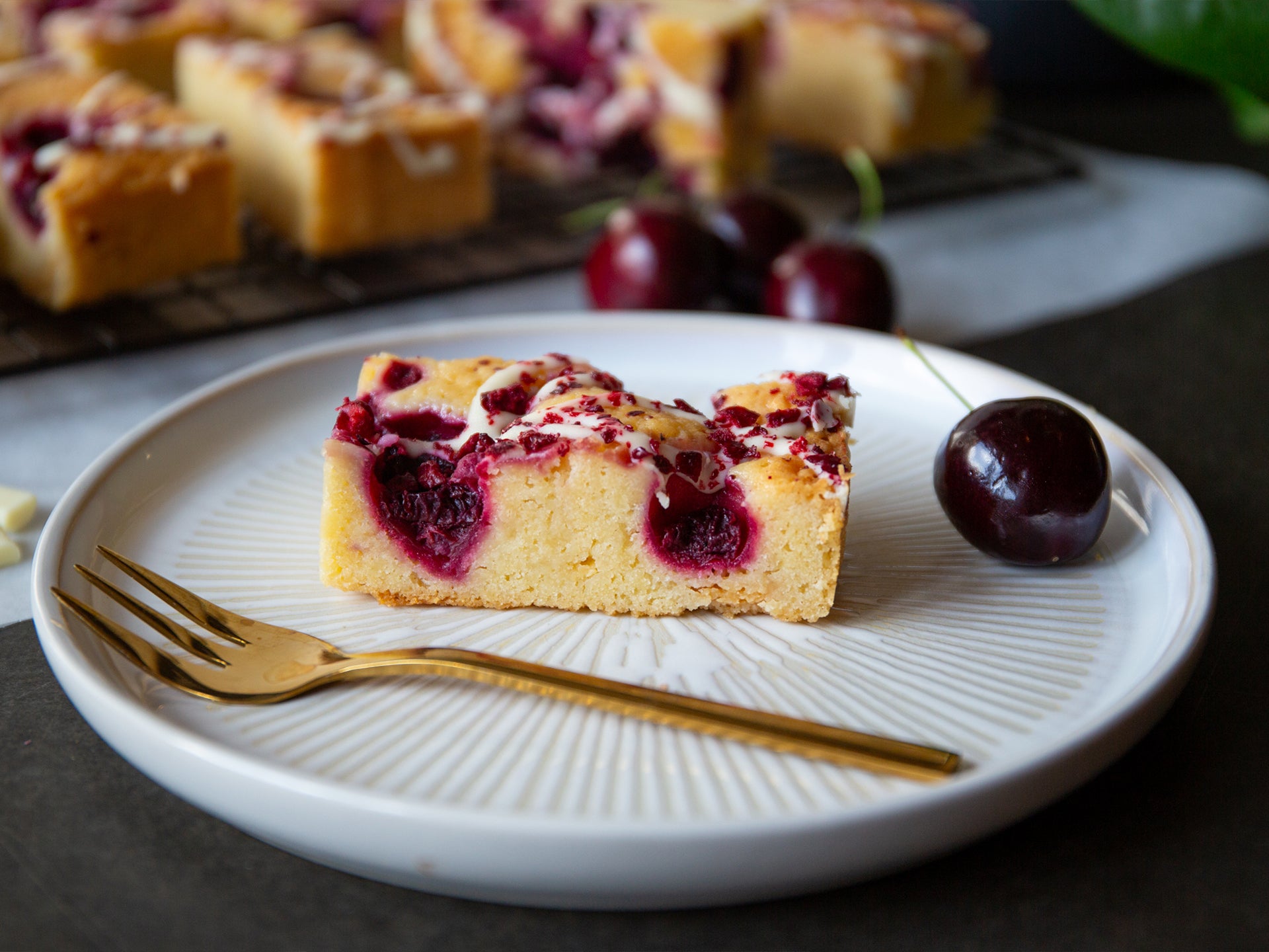 A serving of morello cherry blondie on a plate with a complimentary cherry