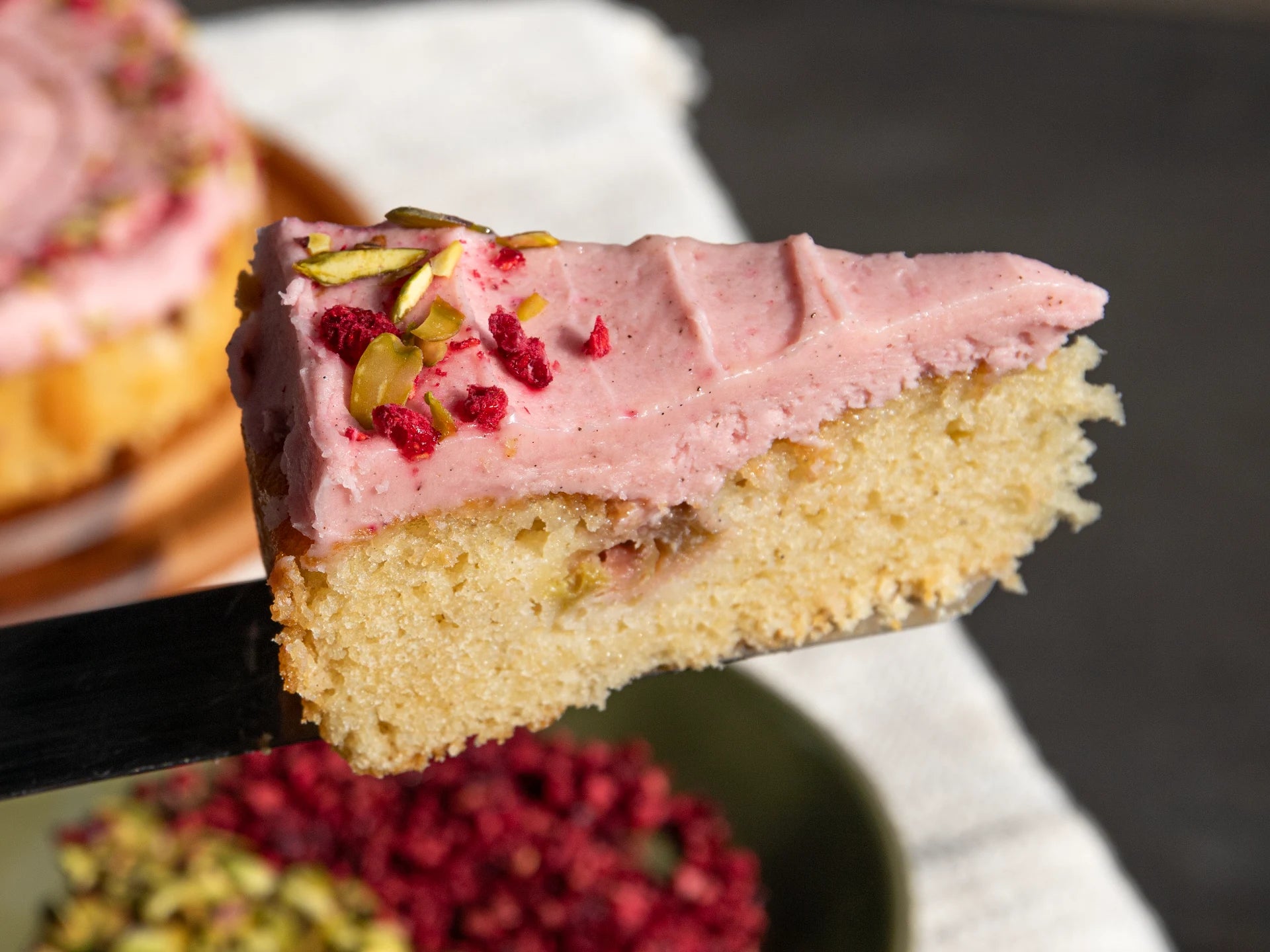 Slice of Raspberry Rhubarb Cake with pink frosting and red berries on a spatula