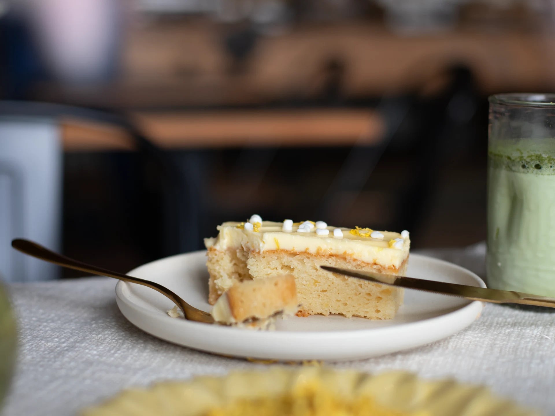 Slice of Sicilian Lemon Meringue cake on a plate with a fork and a green drink in the background