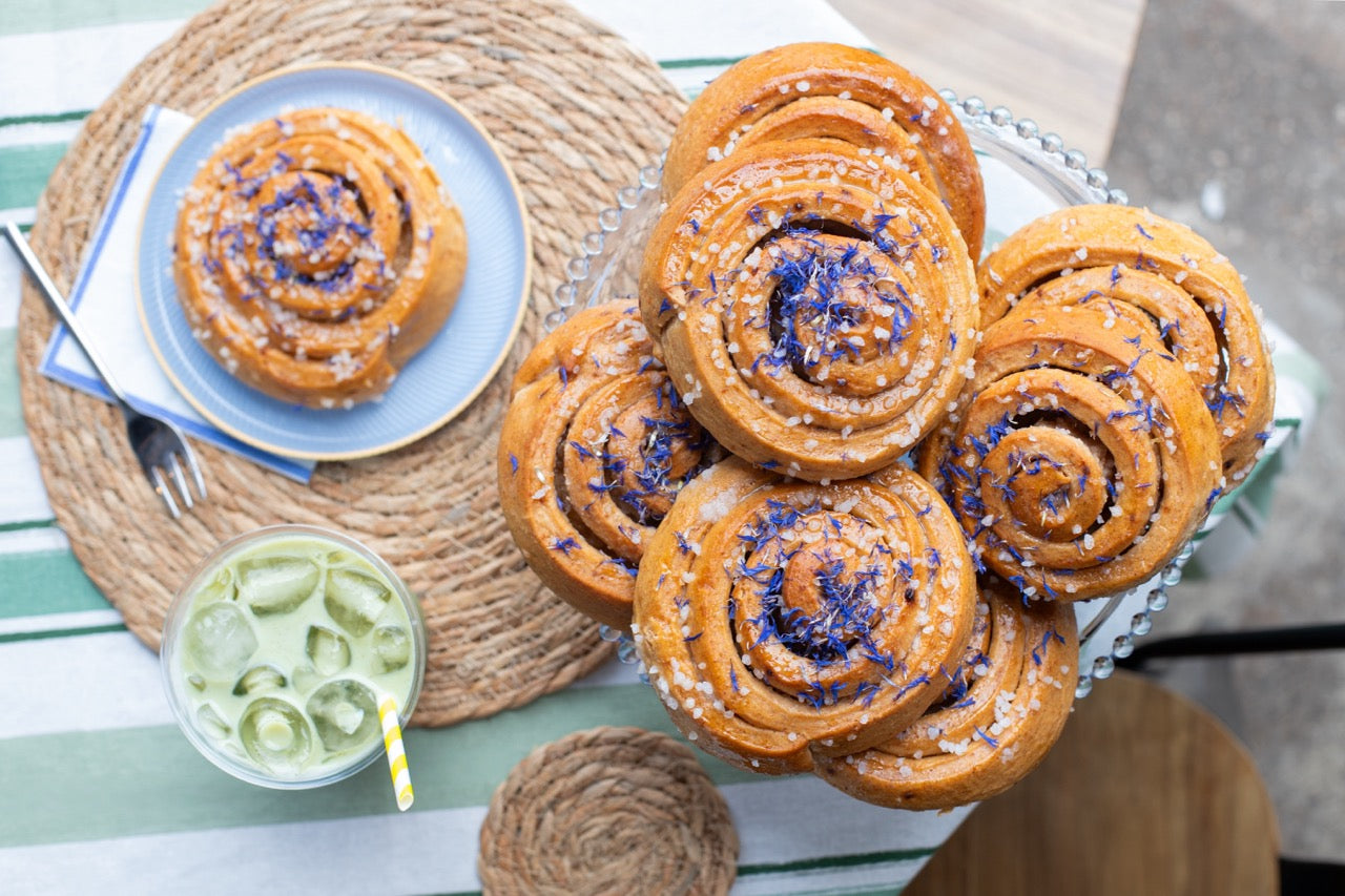 Sticky Lemon Drizzle Buns with blue sprinkles on a tray, accompanied by a glass of lemonade on a table.