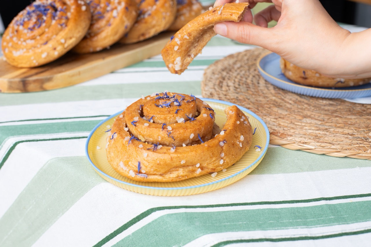 Sticky Lemon Drizzle roll with purple sprinkles on a plate, surrounded by more pastries on a table.