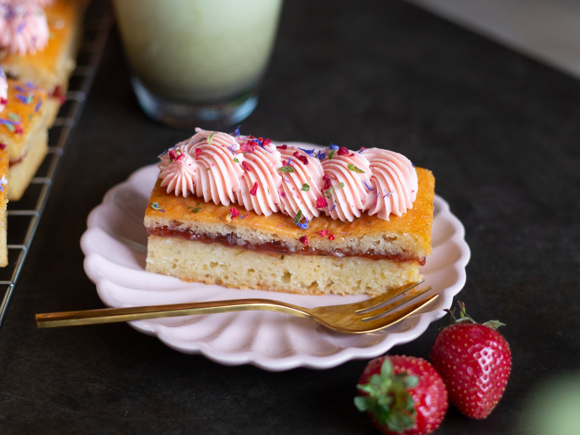 A slice of strawberry cake with pink frosting and edible flowers