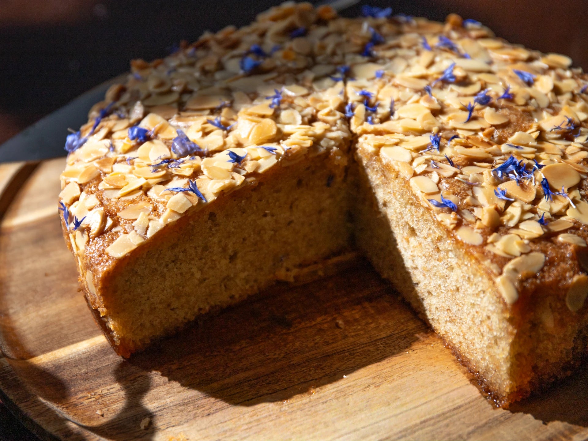 Honey Lavender Almond Round Cake with almonds and blueberries on a wooden cutting board
