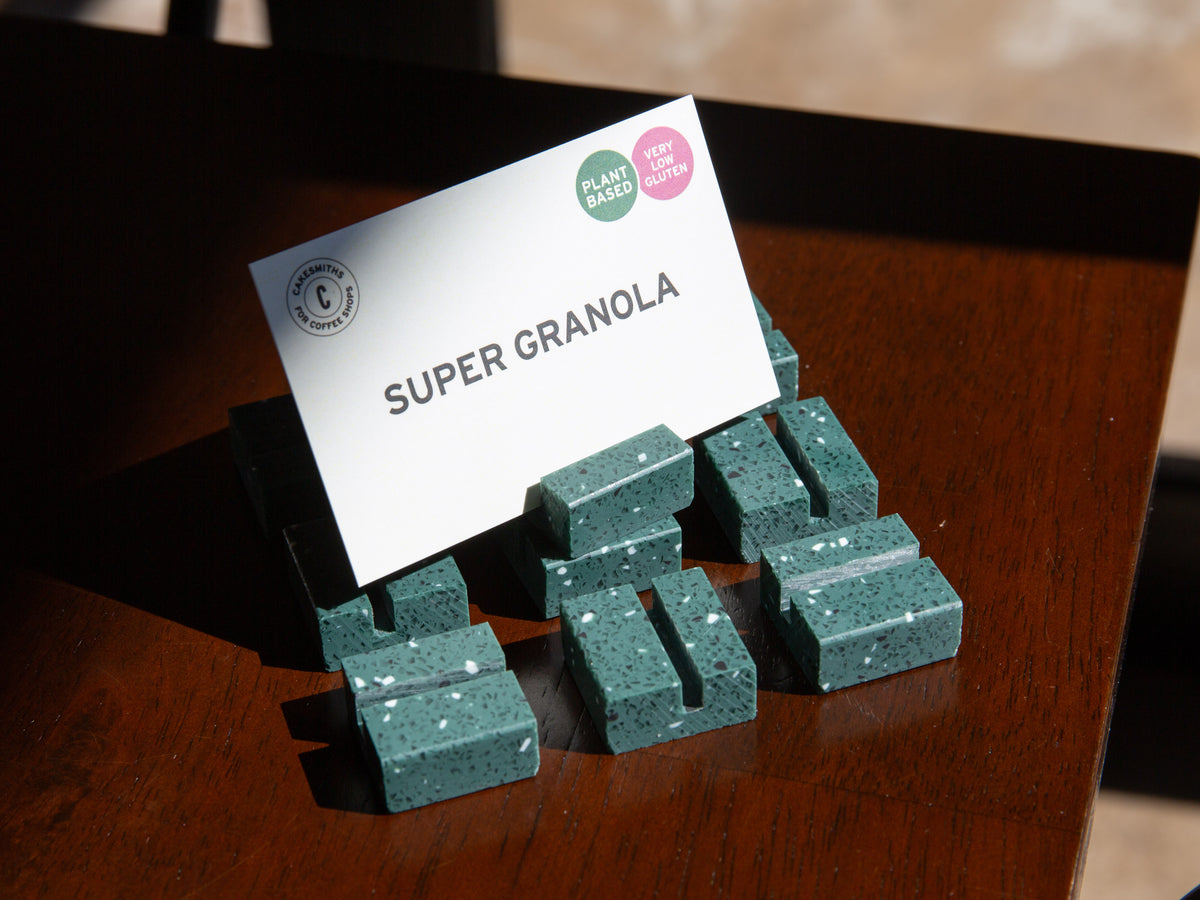Green Green Terrazzo Product Display Card Stands with a card labeled 'Super Granola' on a wooden surface