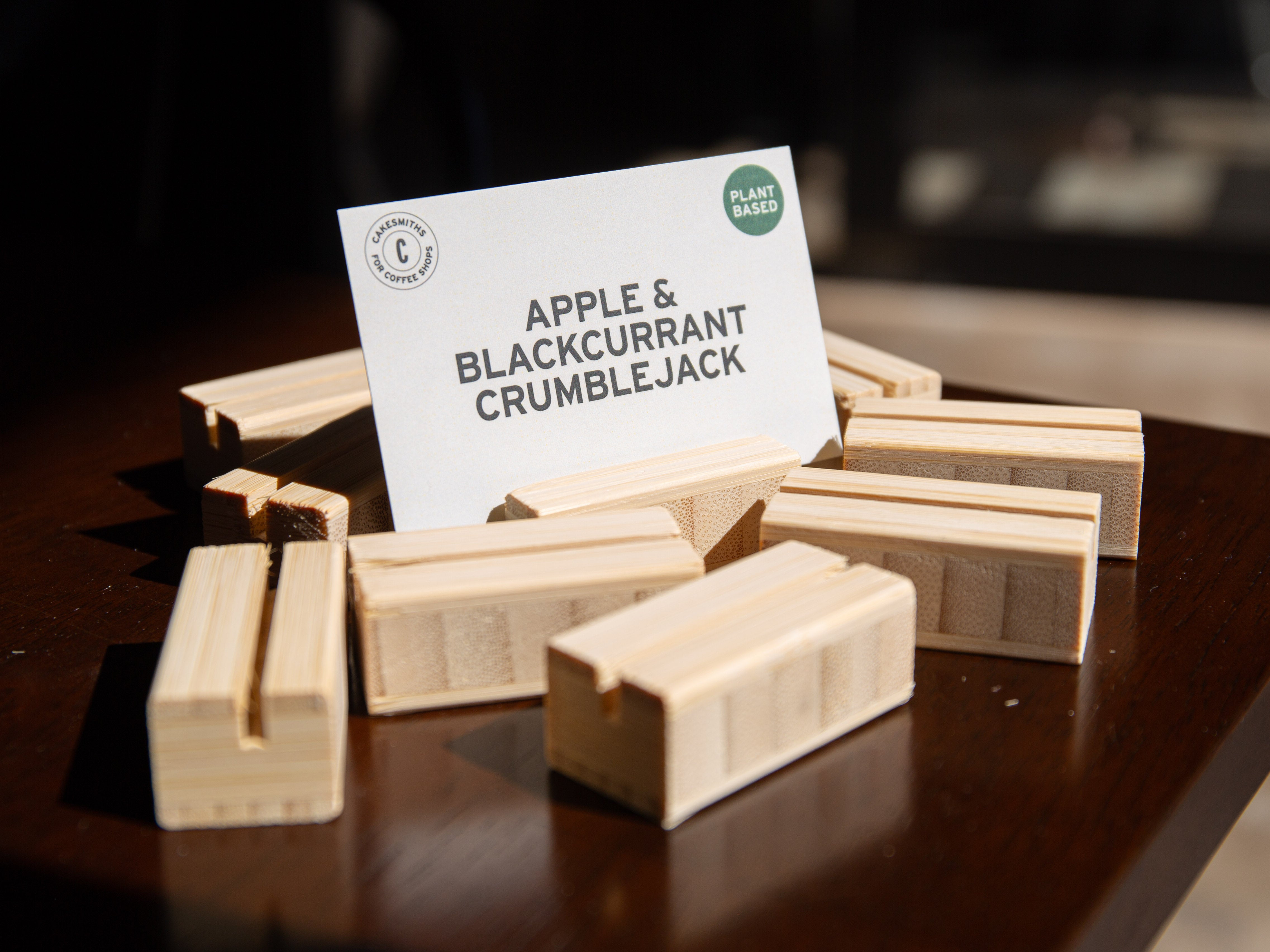 Bamboo Product Display Card Stands blocks with a card labeled 'Apple & Blackcurrant Crumblejack' on a dark surface.