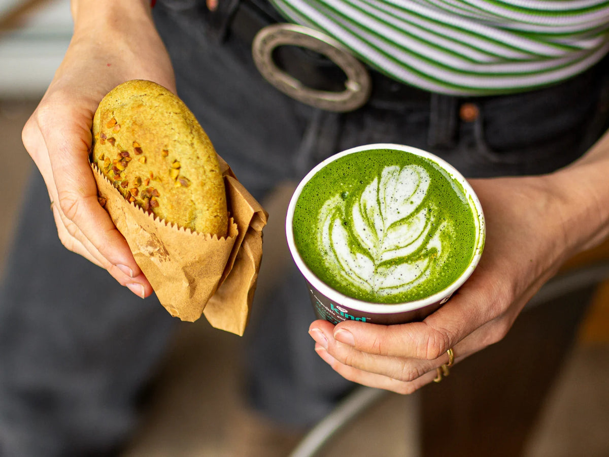 Person holding a green Ceremonial-Quality Wakaba Matcha latte and a pastry