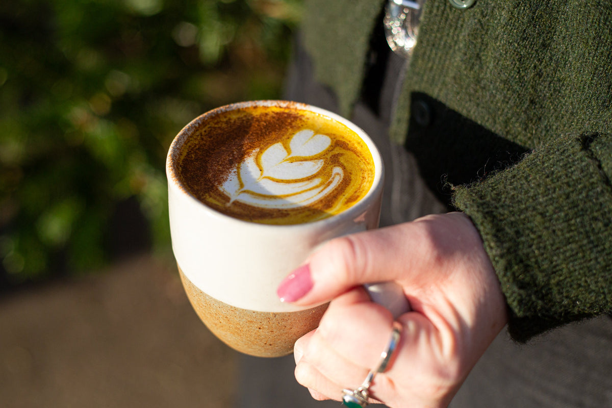 Person holding a cup of coffee with Chai Blendsmiths latte art outdoors