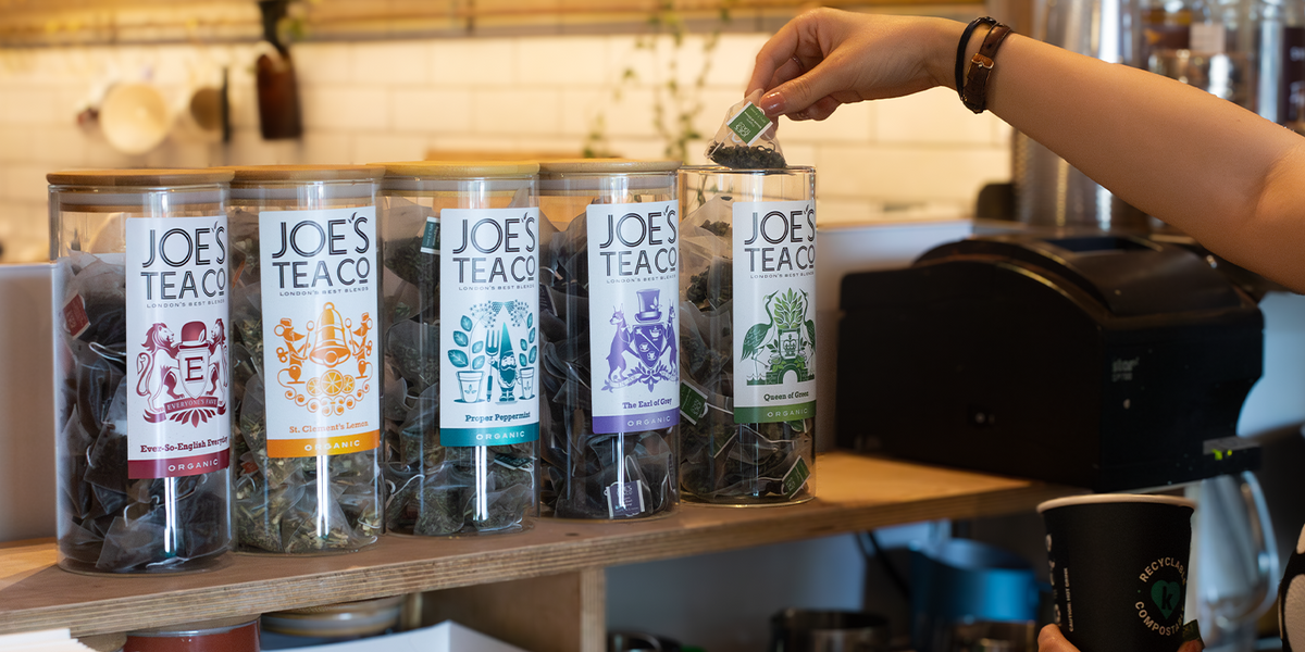 Person selecting a jar of Joe's Tea from a display with various flavors.