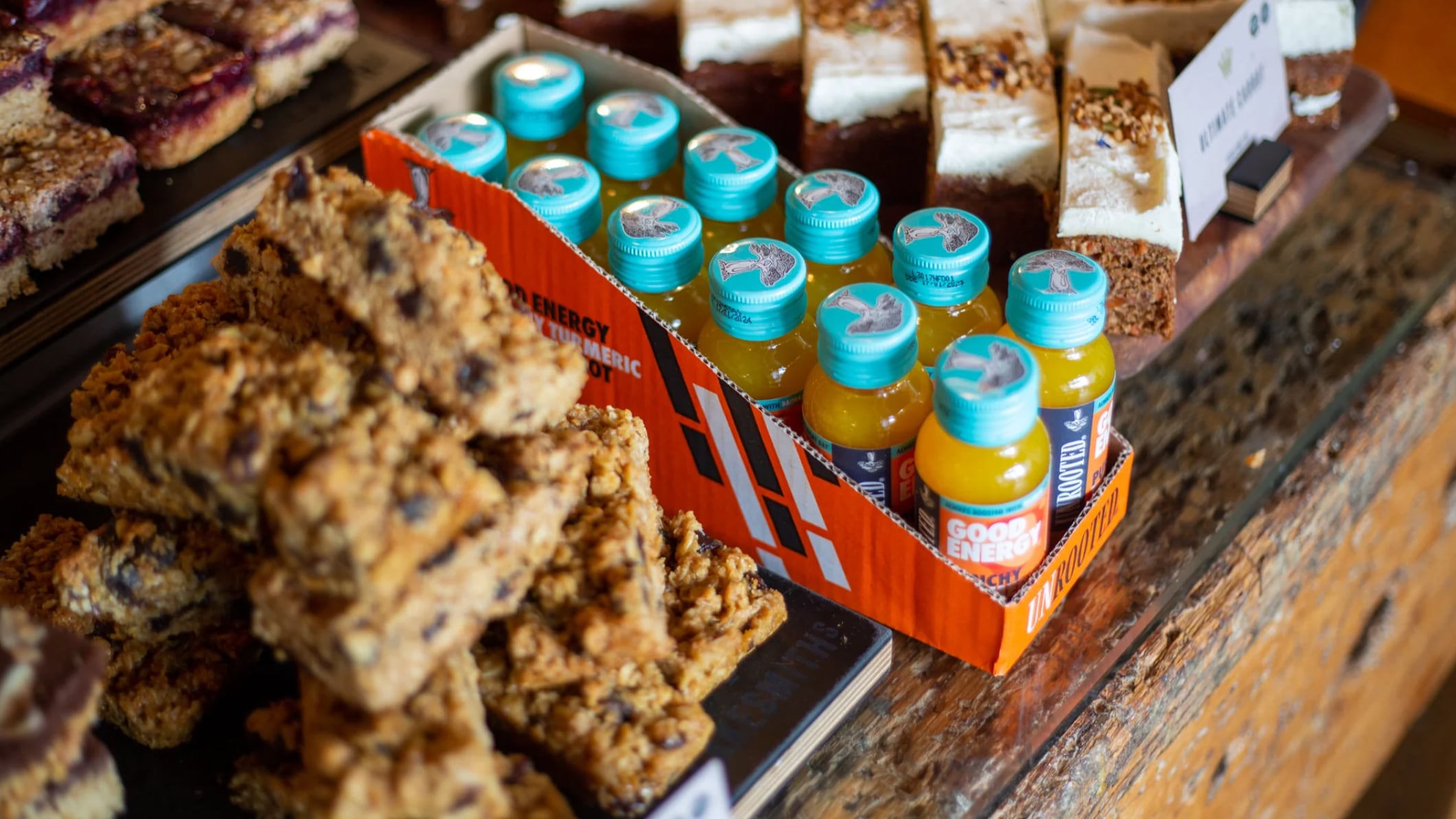 Unrooted Health Shots boxe next to a display of cookies on a wooden shelf.