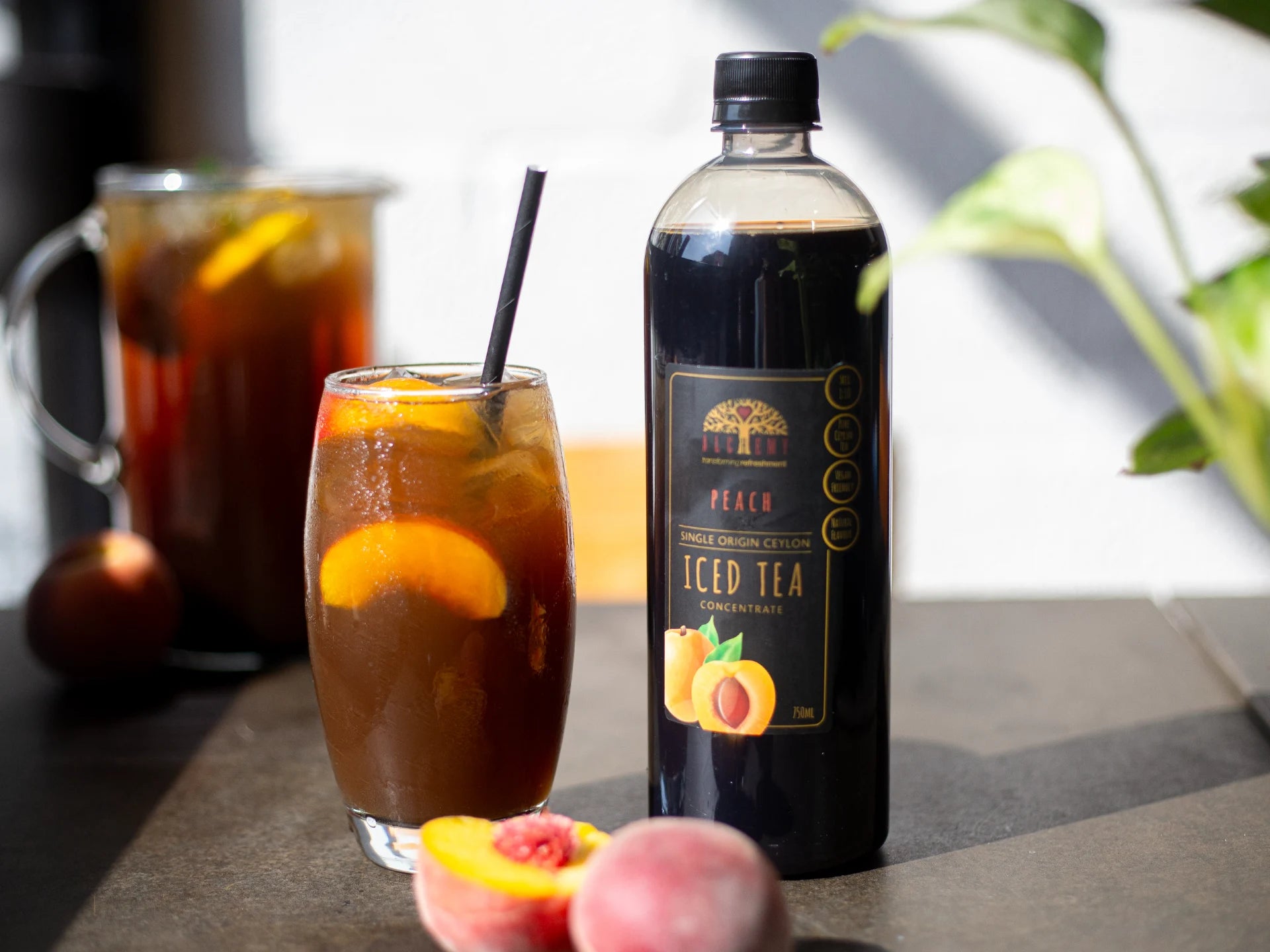 Alchemy Peach iced tea bottle with a glass of iced tea and peaches on a table.