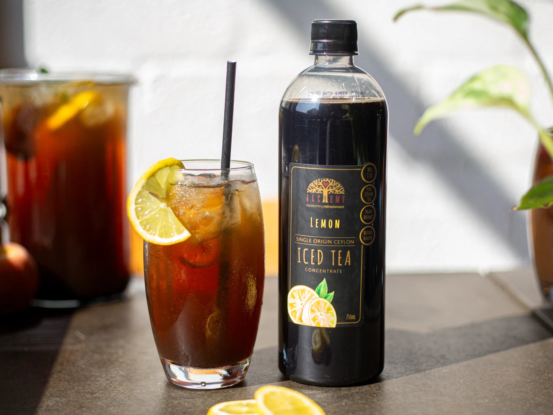 Bottle of Alchemy lemon iced tea with a glass of iced tea and lemon slices on a table.