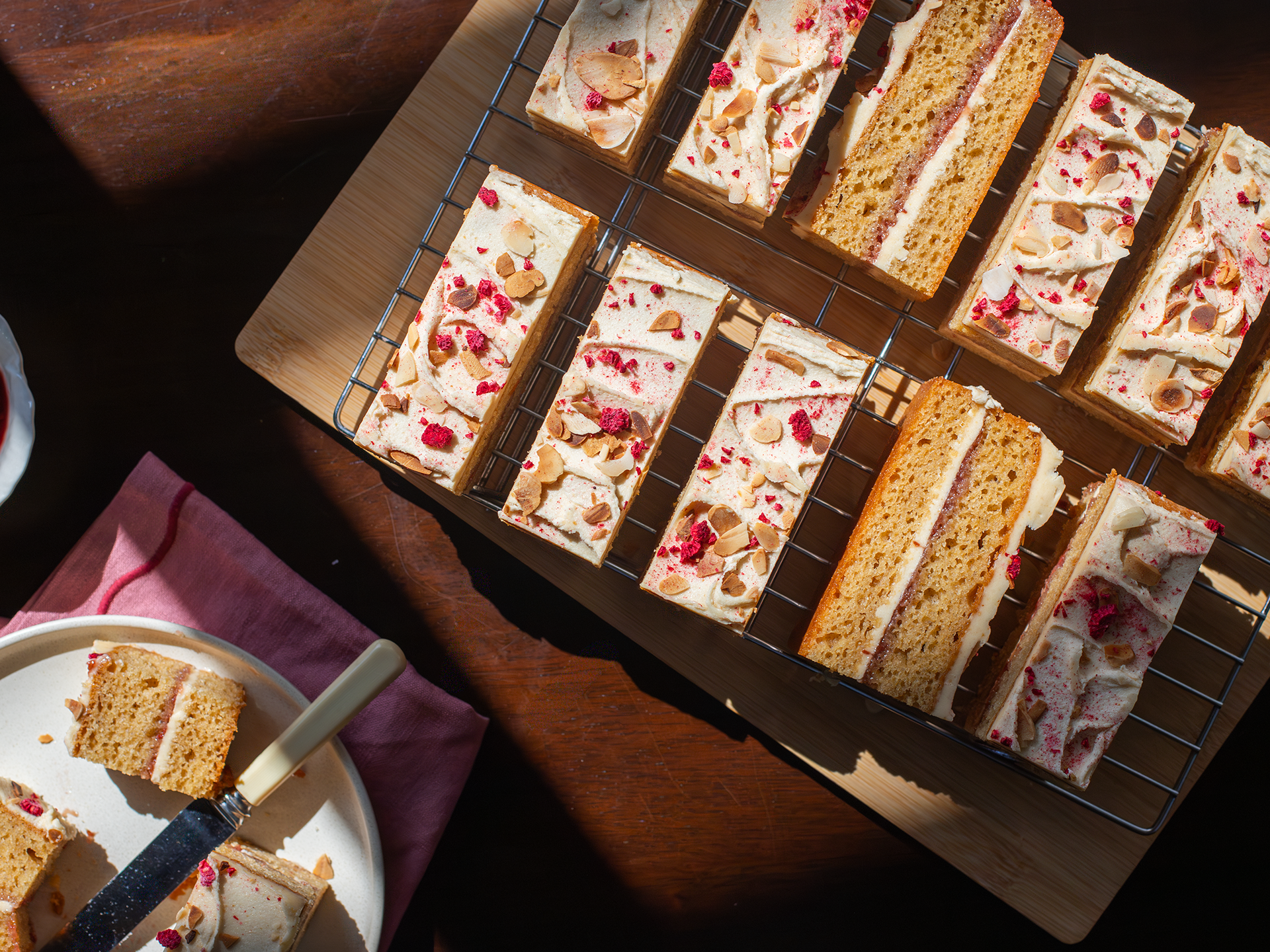 Rectangular slices of Almond Butter and Jelly cake on a cooling rack with a plate and knife on a wooden surface.
