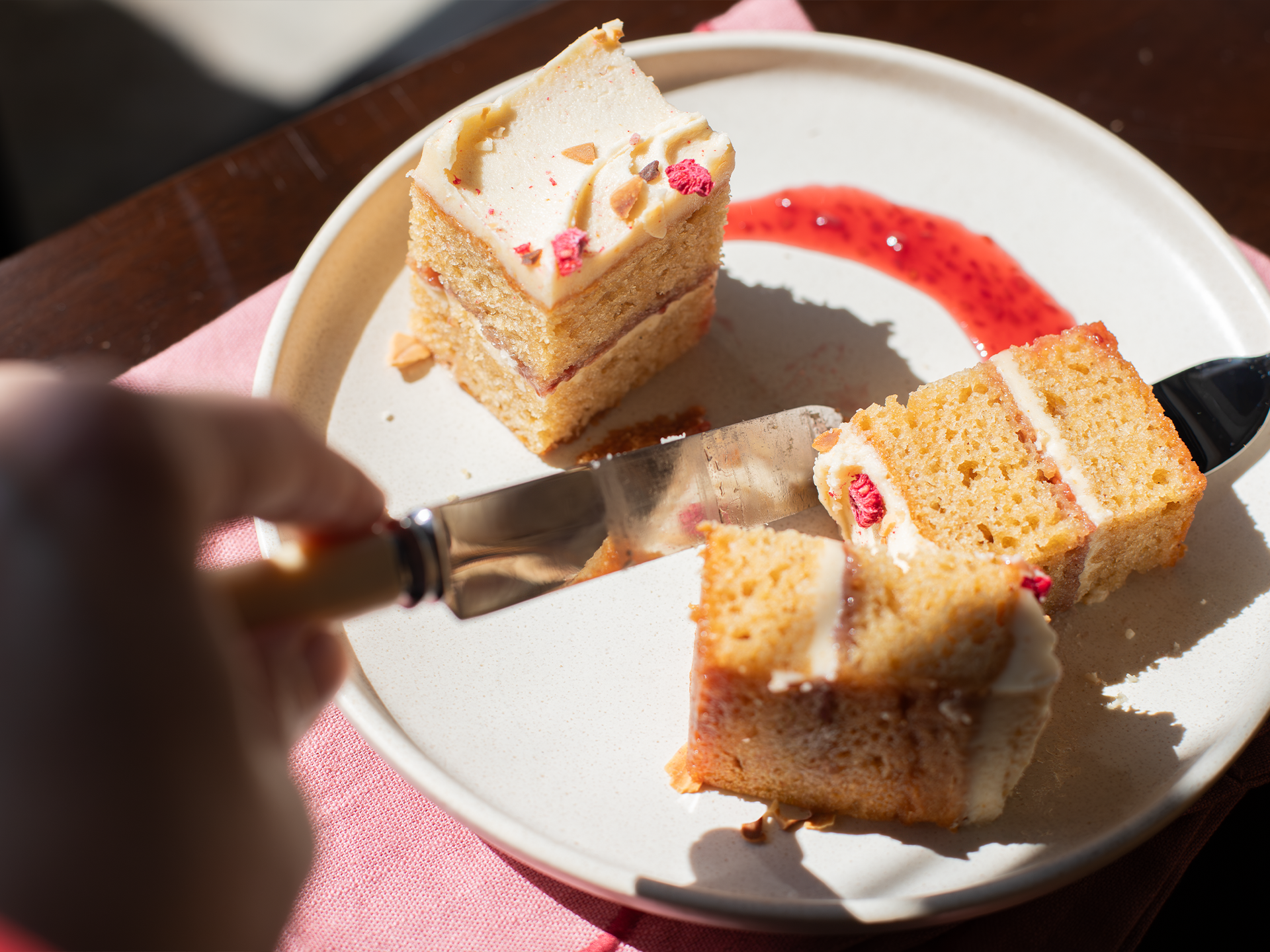 Two slices of Almond Butter and Jelly cake on a plate with a hand holding a knife.