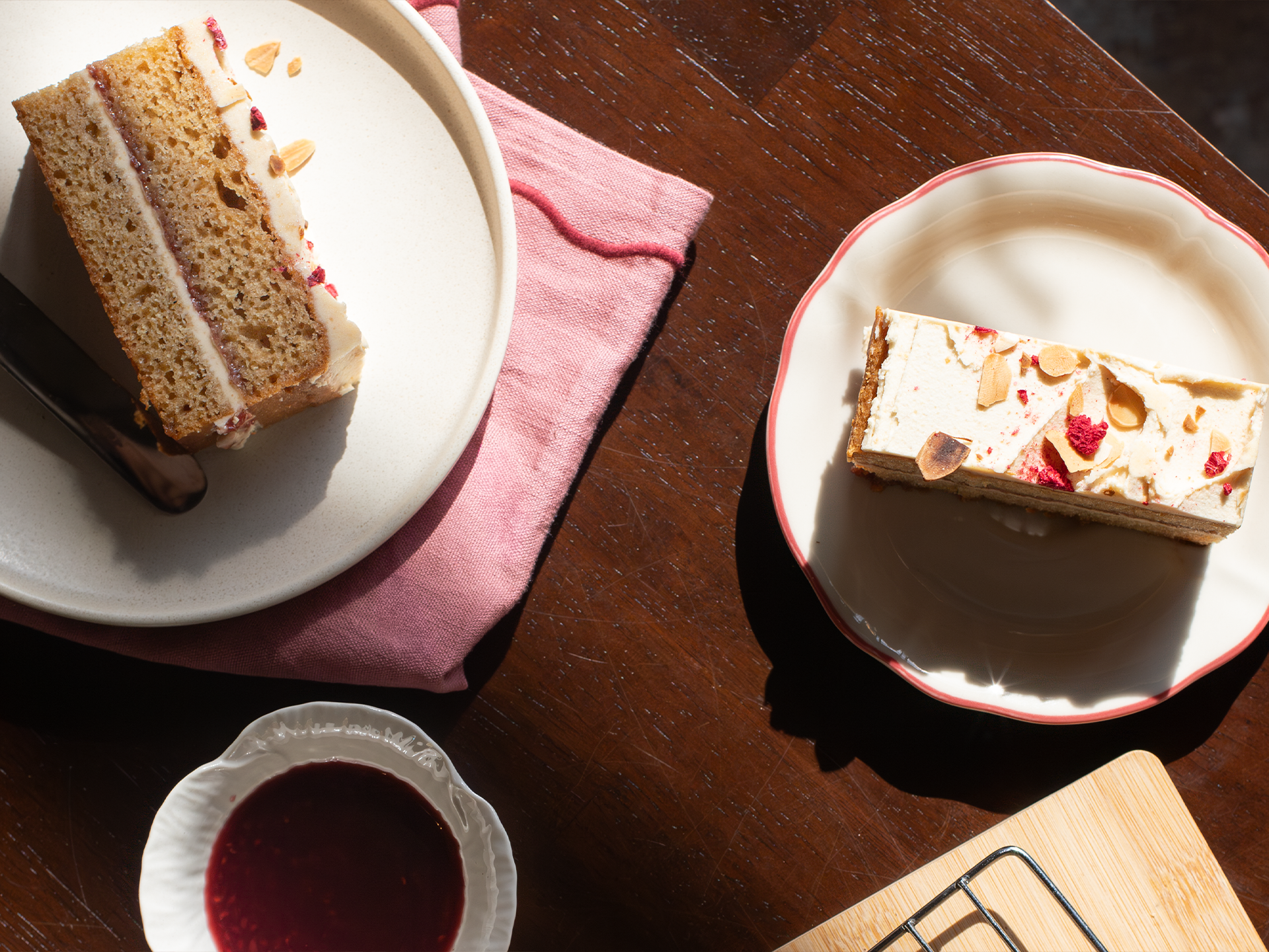 Two slices of Almond Butter and Jelly cake on white plates with a pink napkin on a wooden table.