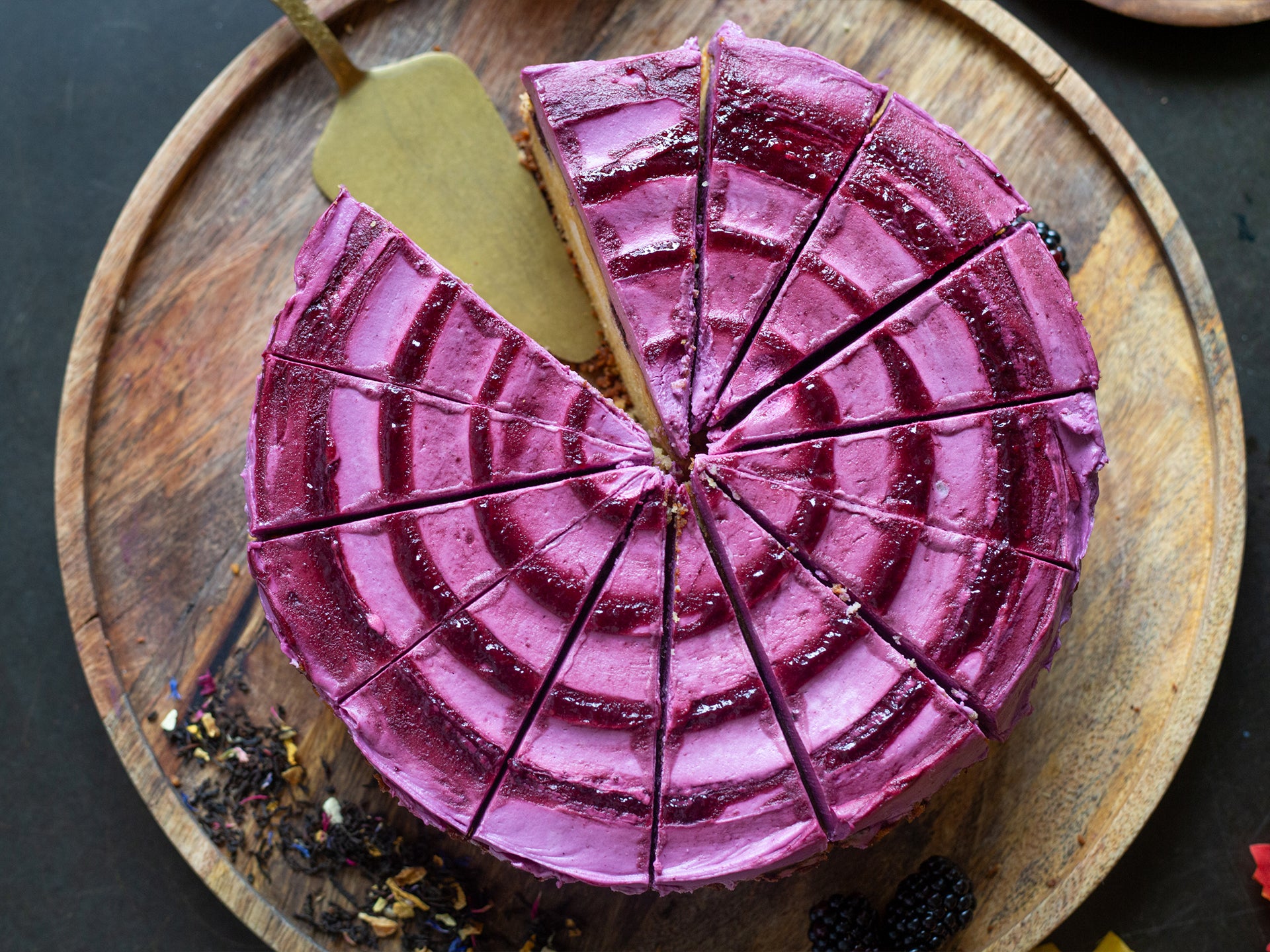 Purple blackberry round cake with a slice cut out on a wooden board