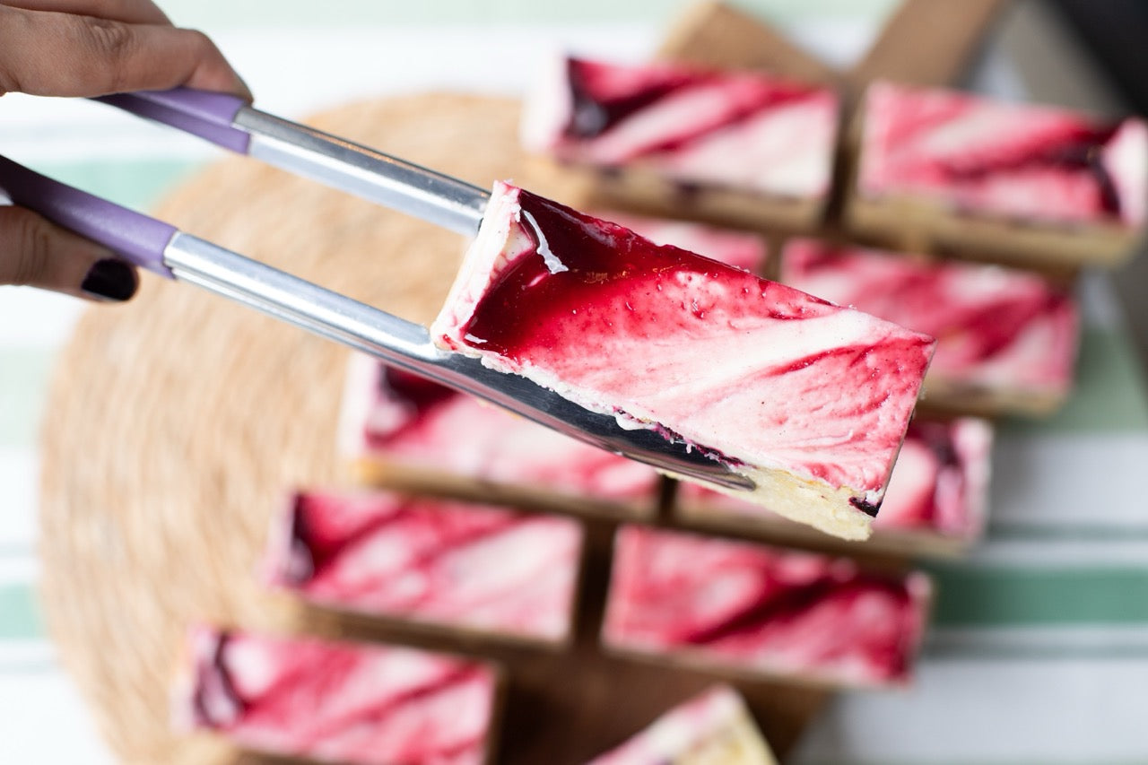 Red jelly Blackcurrant Ripple dessert being held with chopsticks against a blurred background of more desserts.