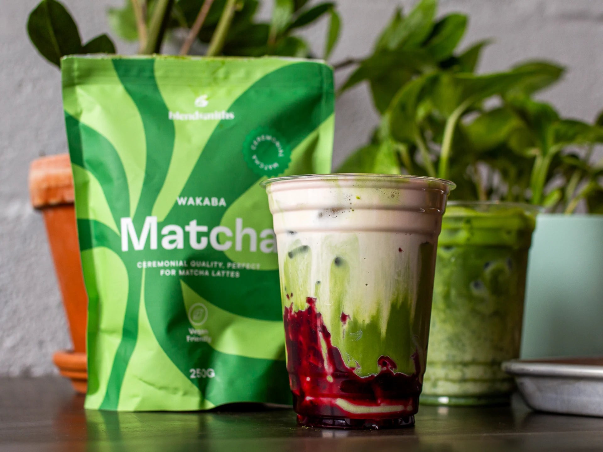 Ceremonial-Quality Wakaba Matcha powder package with a matcha latte in a clear cup against a plant-filled background