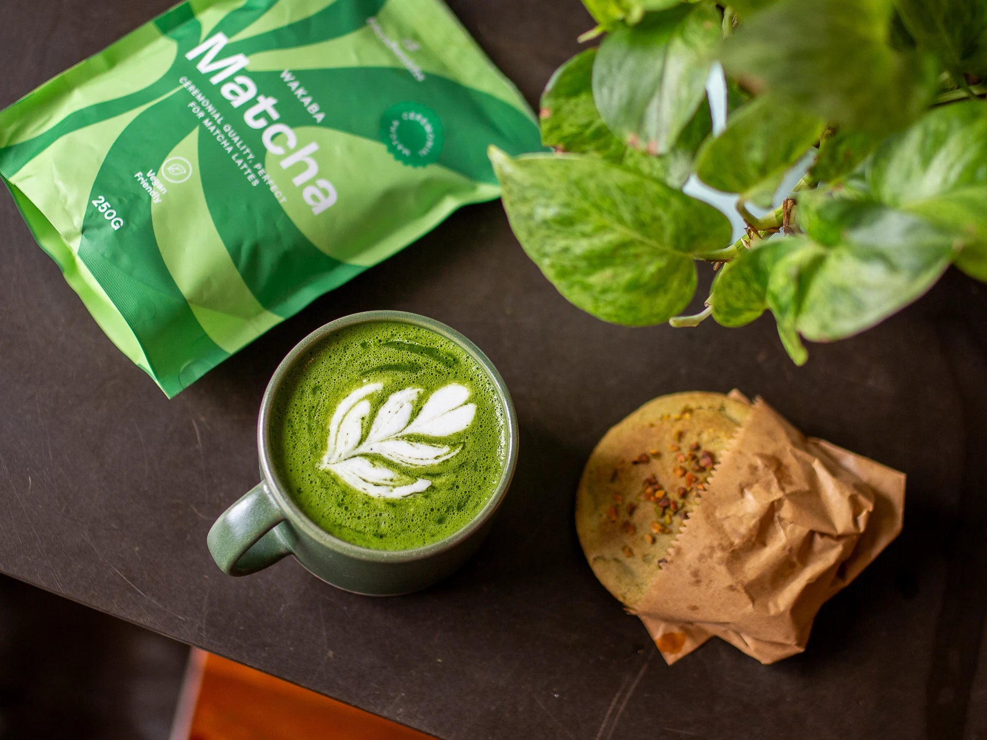 Ceremonial-Quality Wakaba Matcha green tea in a cup with a packet of matcha and a cookie on a dark surface.