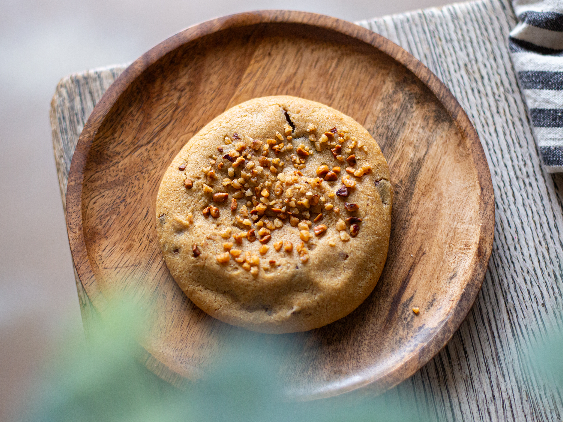 Wholesale Cookie with hazelnut nibs on a wooden plate on a textured surface