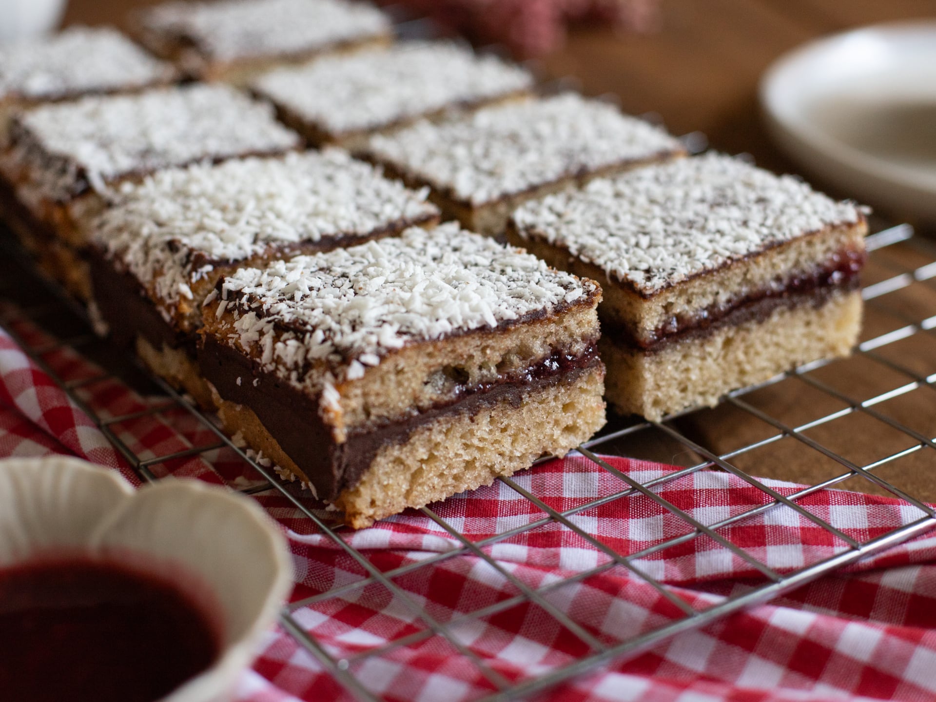 Chocolate Raspberry Lamington Cake  bars with a layer of jam and coconut on top, placed on a cooling rack.