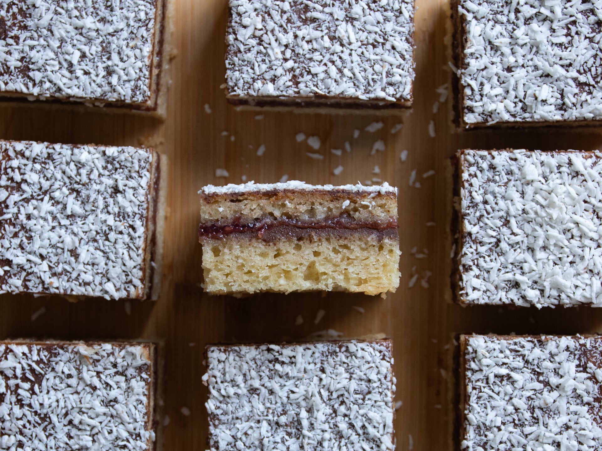 Sliced layered Chocolate Raspberry Lamington Cake with a jam filling on a wooden board