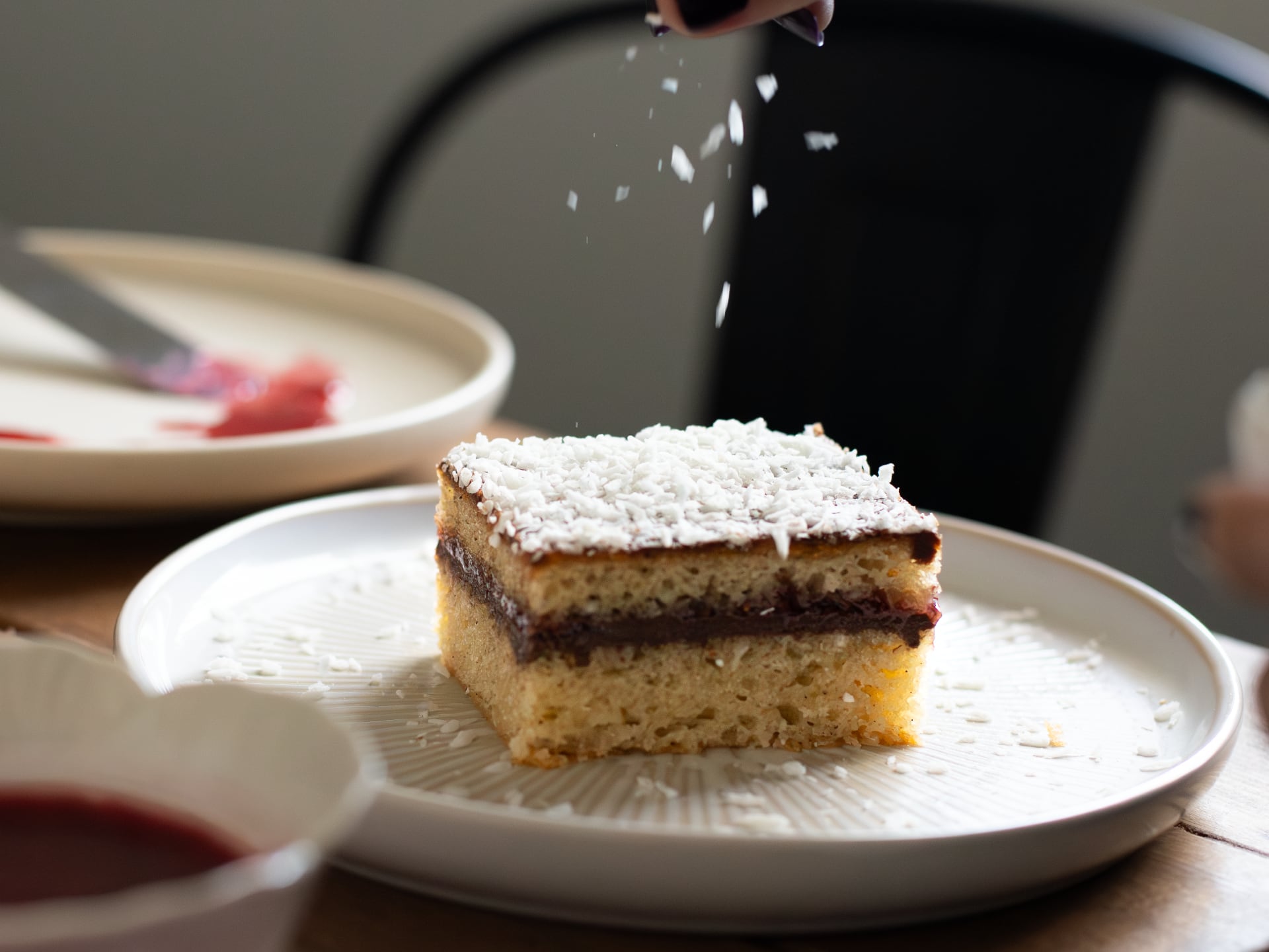 Slice of layered Chocolate Raspberry Lamington Cake  on a plate with powdered sugar being sprinkled over it.