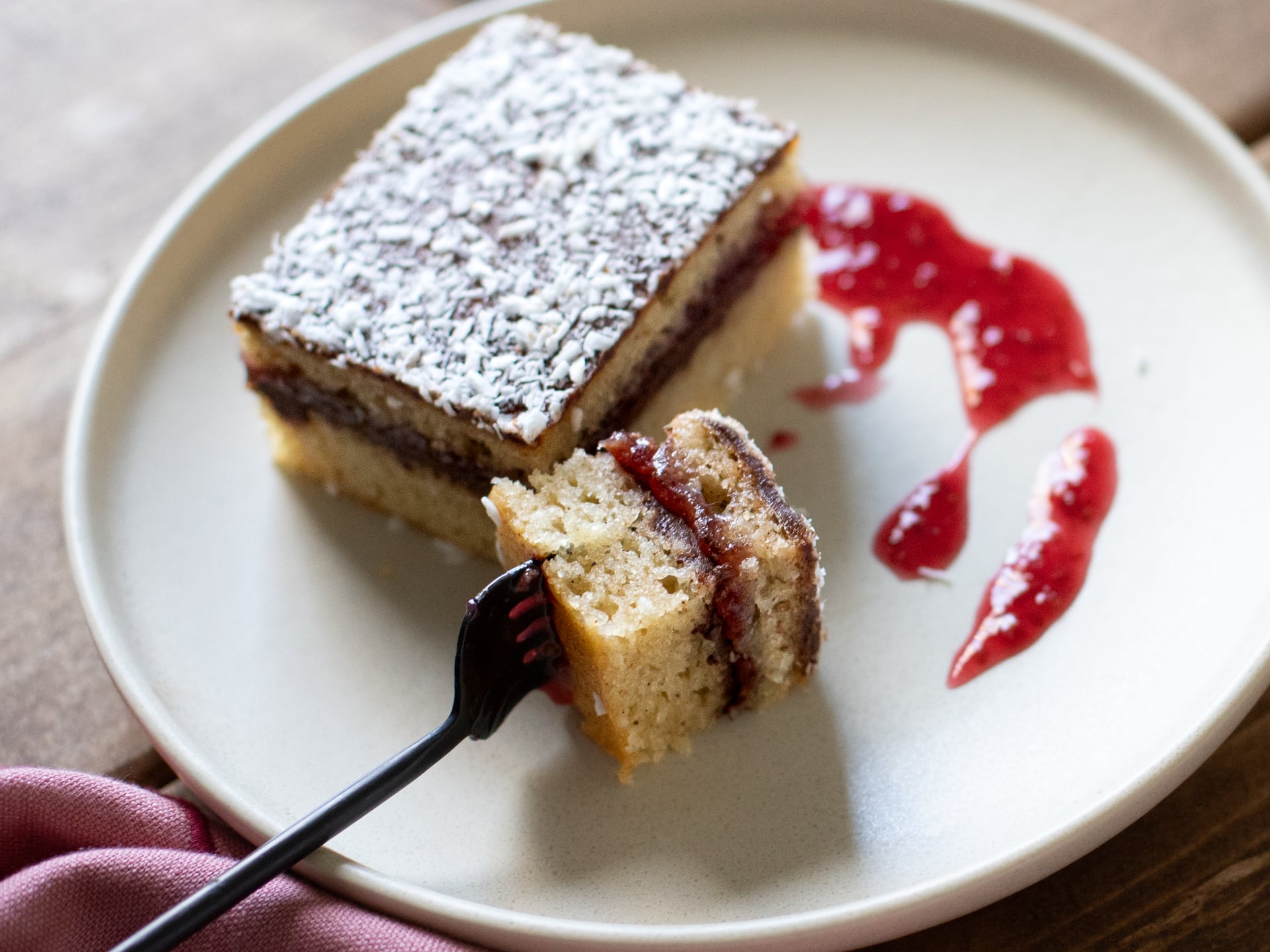 Slice of Chocolate Raspberry Lamington Cake  with coconut on a plate with strawberry sauce