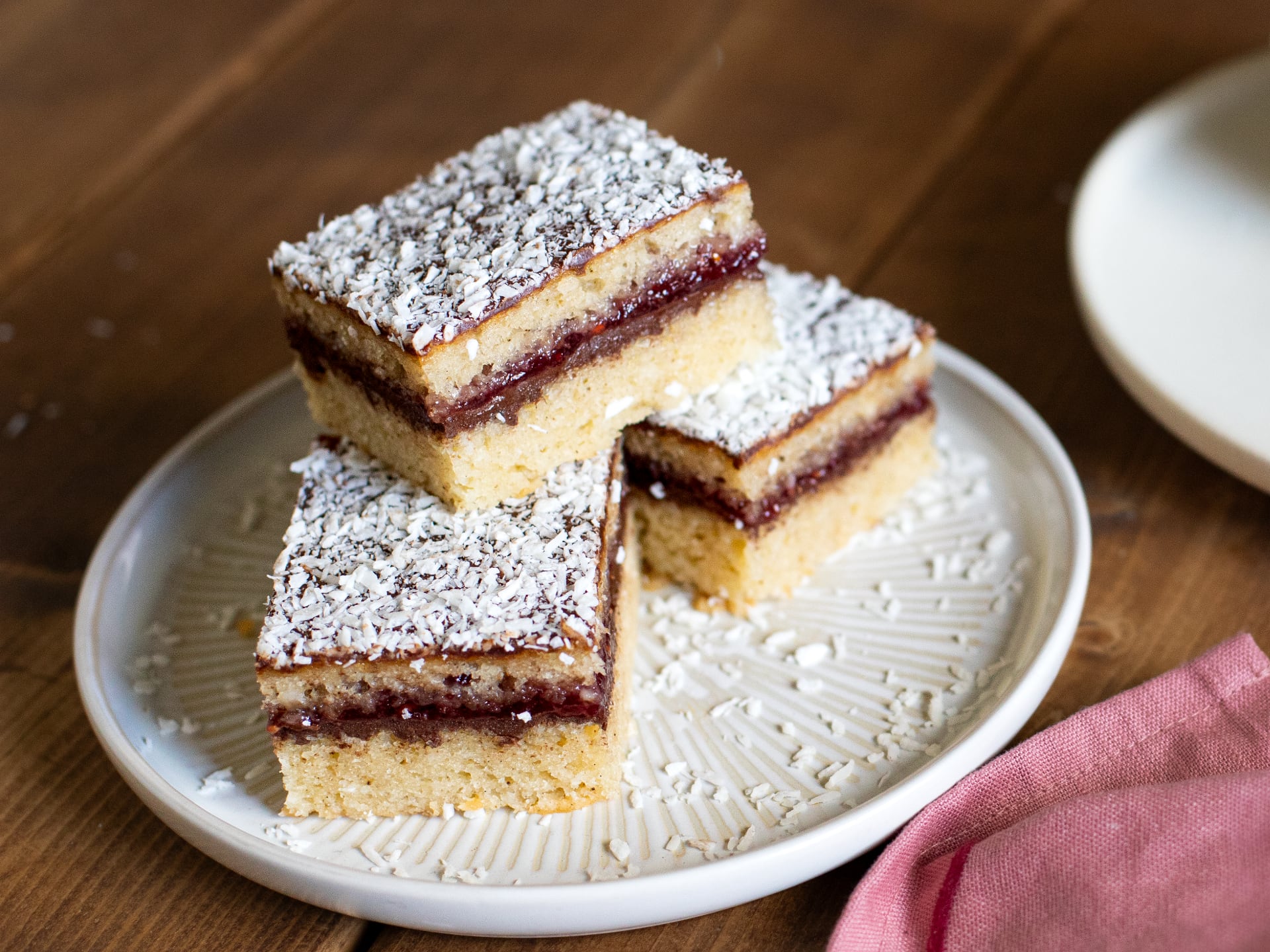 Three square slices of Chocolate Raspberry Lamington Cake  on a decorative white plate with a wooden background.