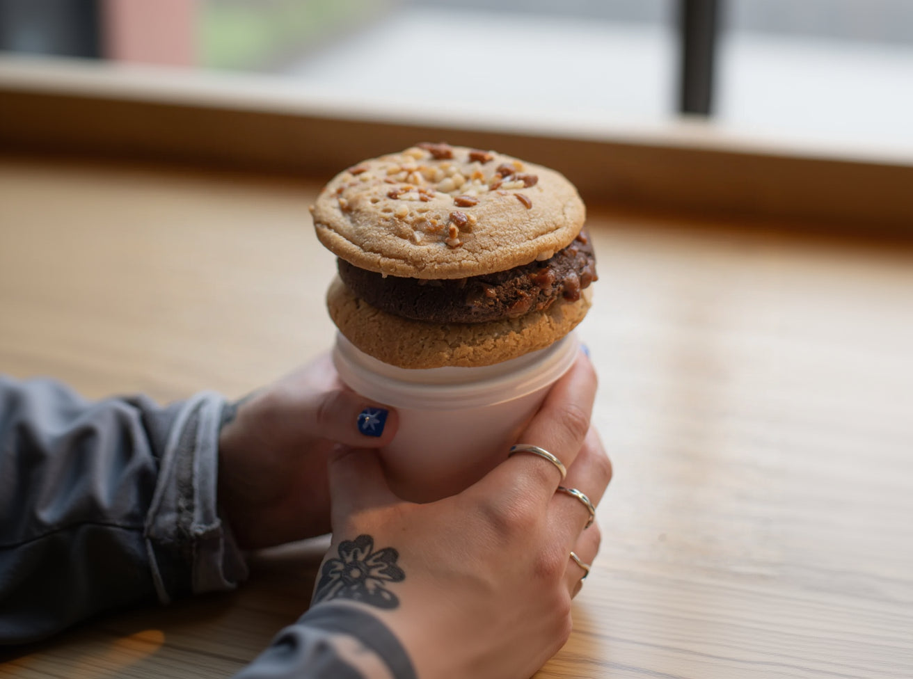 Hand holding a cookie sandwich in a white container on a wooden surface