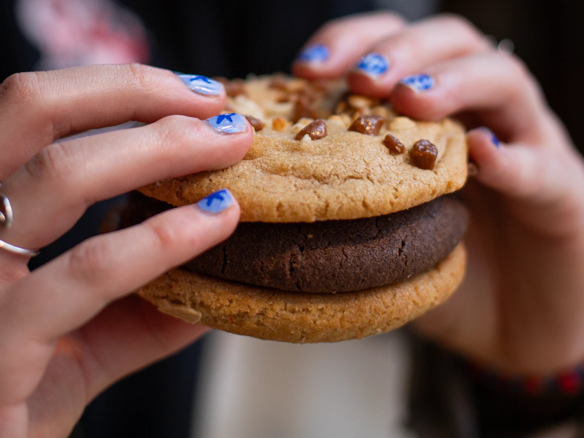 Two hands holding a stack of chocolate and vanilla cookies with nuts.