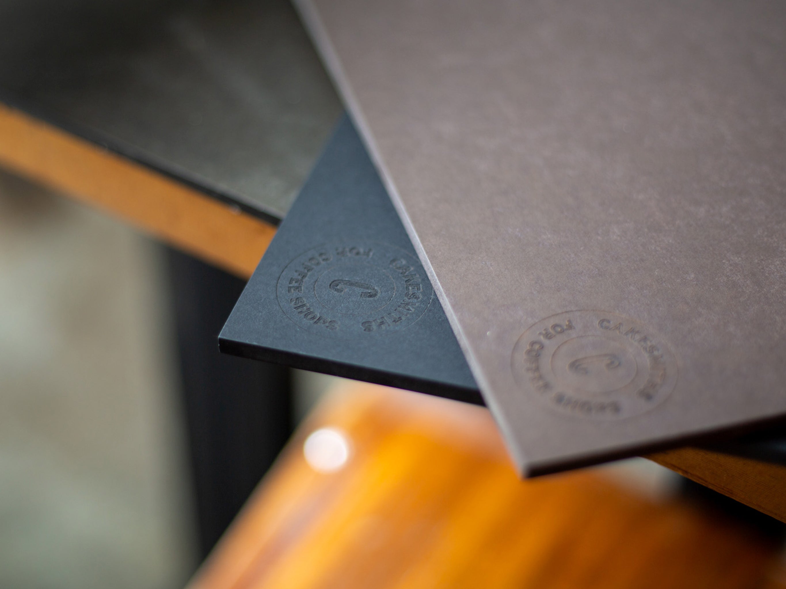 A close-up of a dark-colored cake display board with a branded embossed design, placed on a wooden surface.