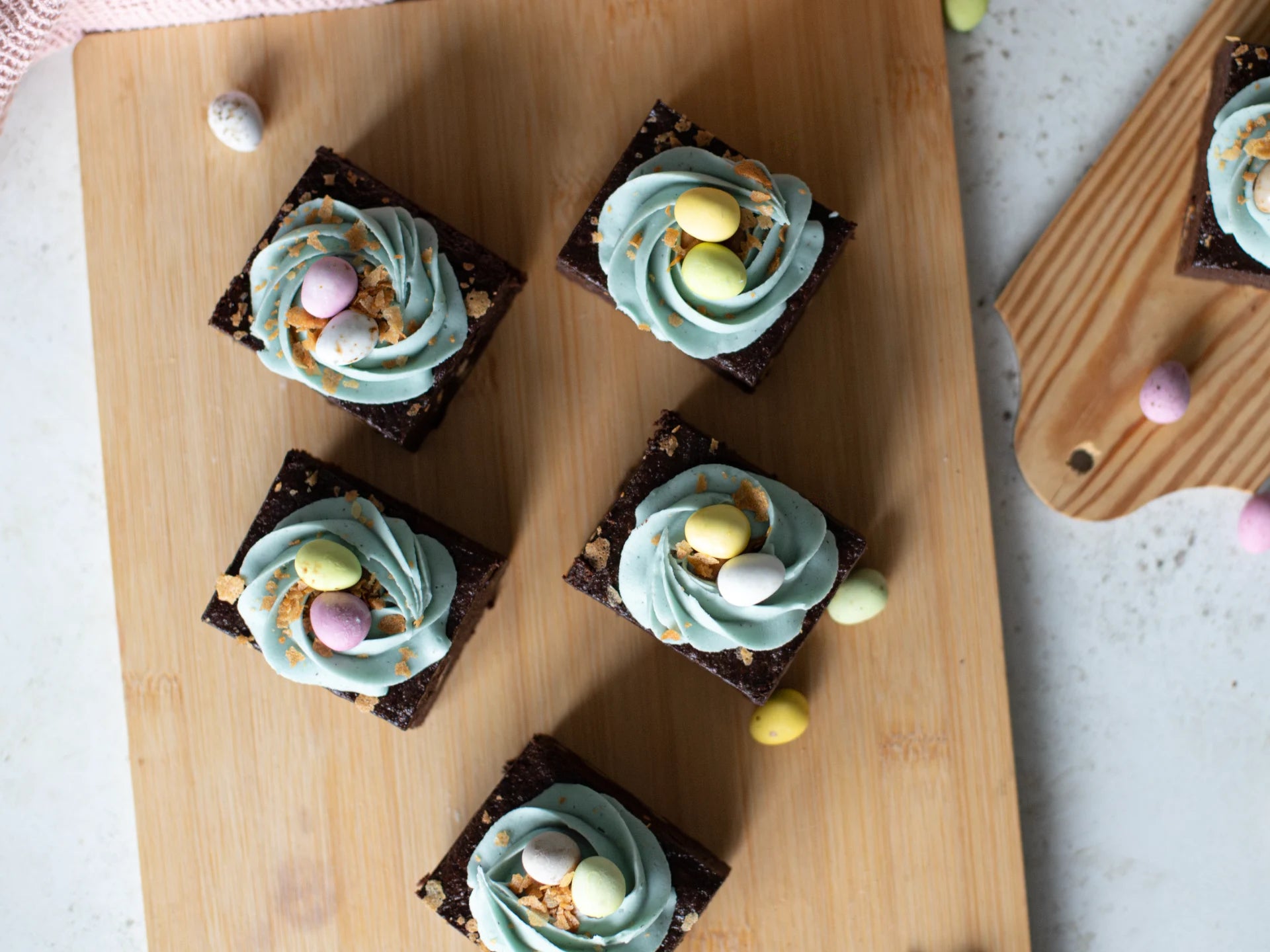 Brownies with Chocolate Easter Nest Cake blue  frosting and colorful Easter eggs on a wooden board.
