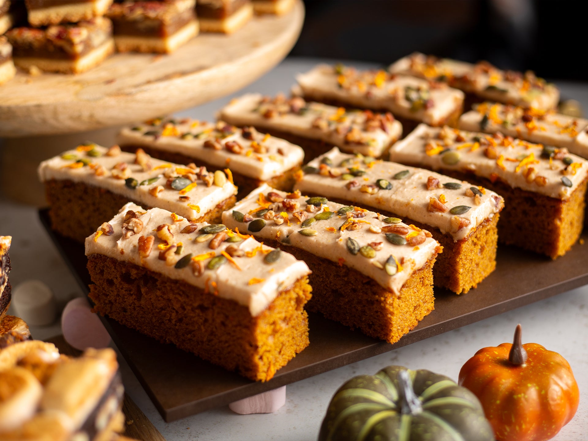 Pumpkin and maple traycake slices with cream cheese frosting on a wooden board, surrounded by small pumpkins.