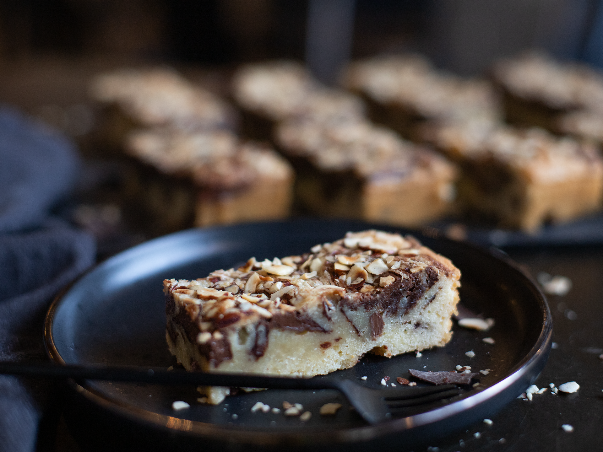 Slice of Hazelnut Blondie cake with nuts on a black plate, blurred background
