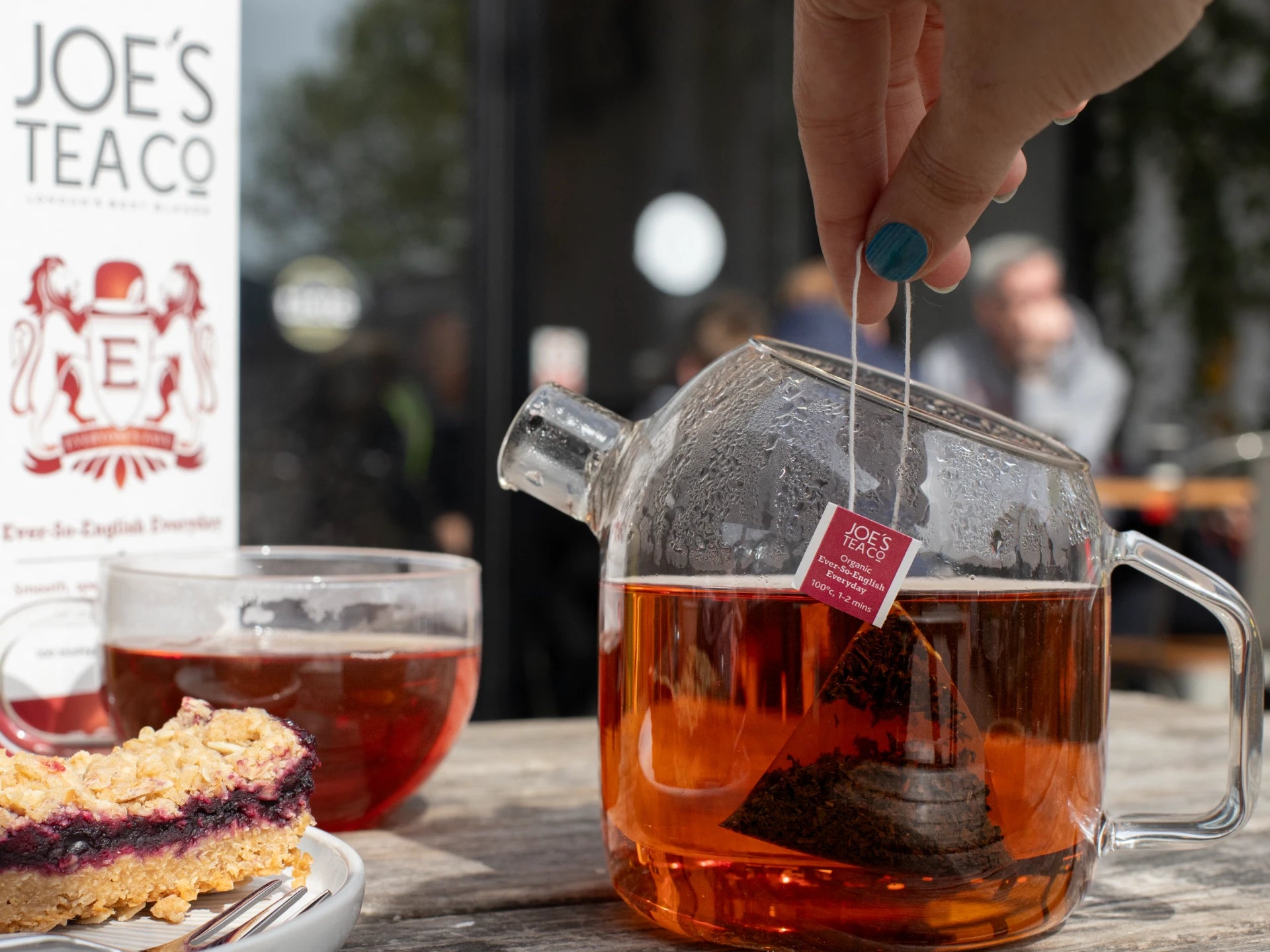 Person pouring tea into a glass teapot with JOE'S TEA CO. branding in the background.