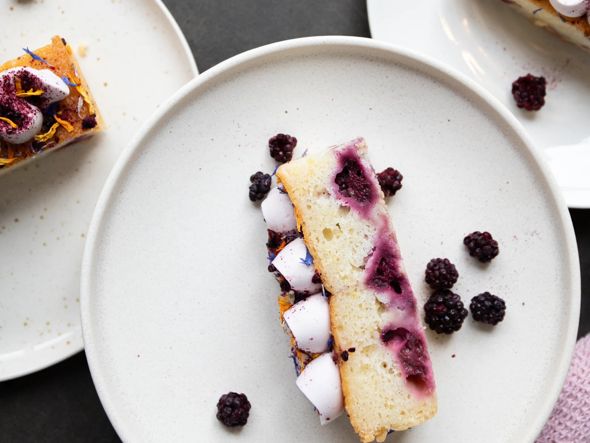 Sliced Lemon Blackberry Elderflower cake with blackberry filling on a white plate with scattered blackberries.