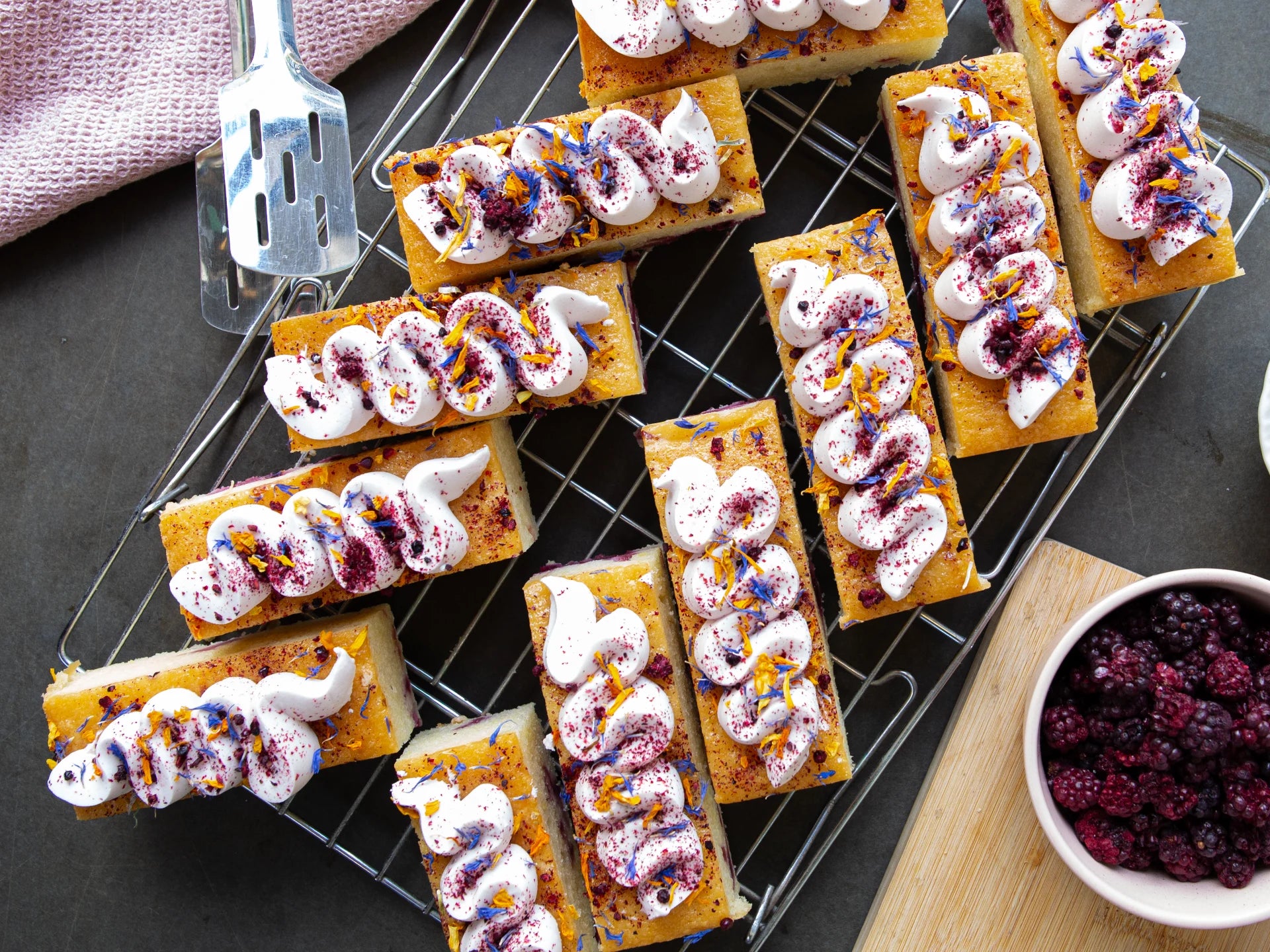 Small rectangular Lemon Blackberry Elderflower cake with white cream and colorful toppings on a cooling rack.