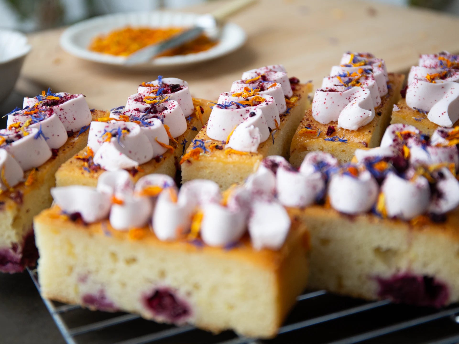 Sliced Lemon Blackberry Elderflower  cake with white frosting and colorful toppings on a cooling rack.
